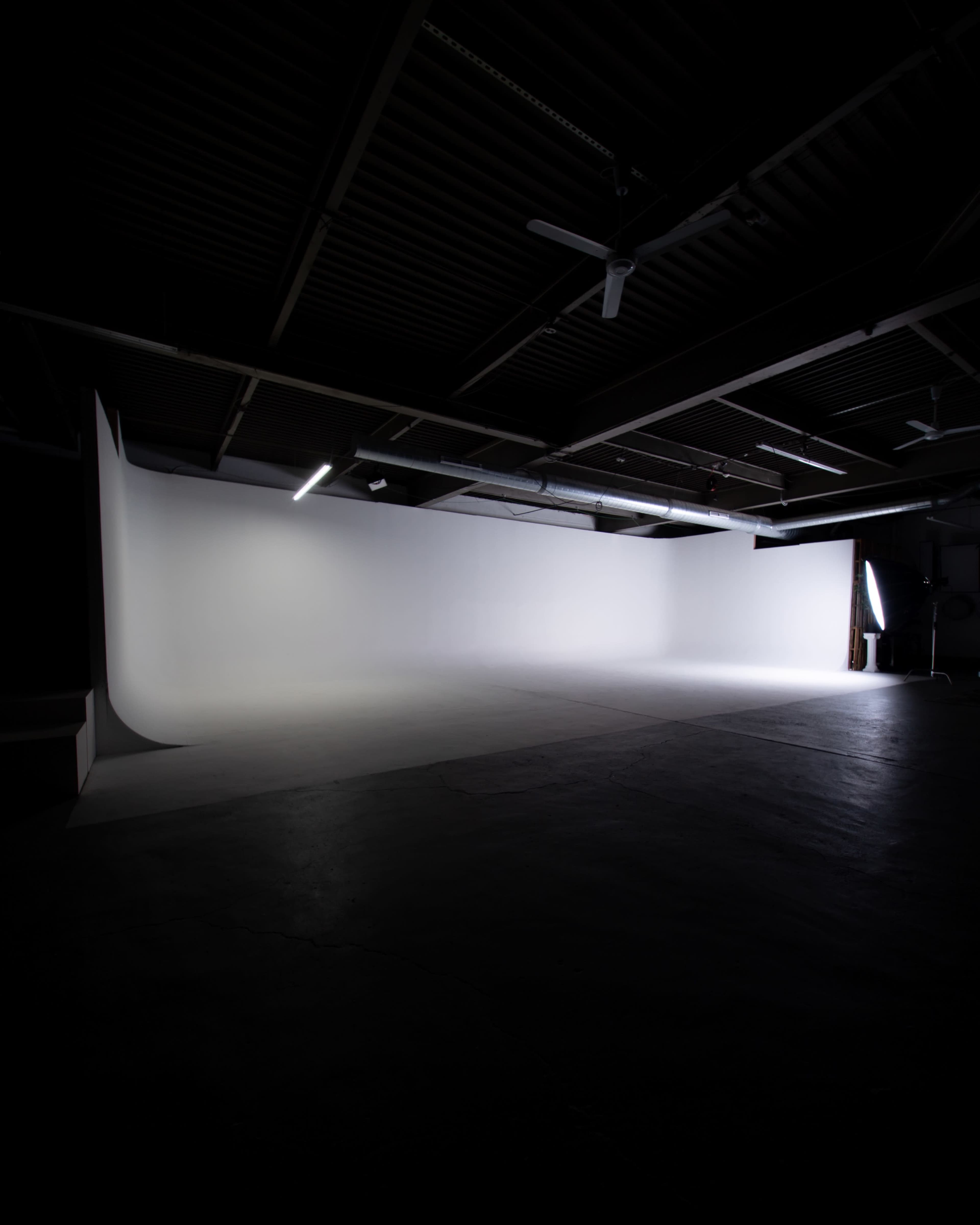 The image shows a dimly lit photography studio with a large, white seamless backdrop.