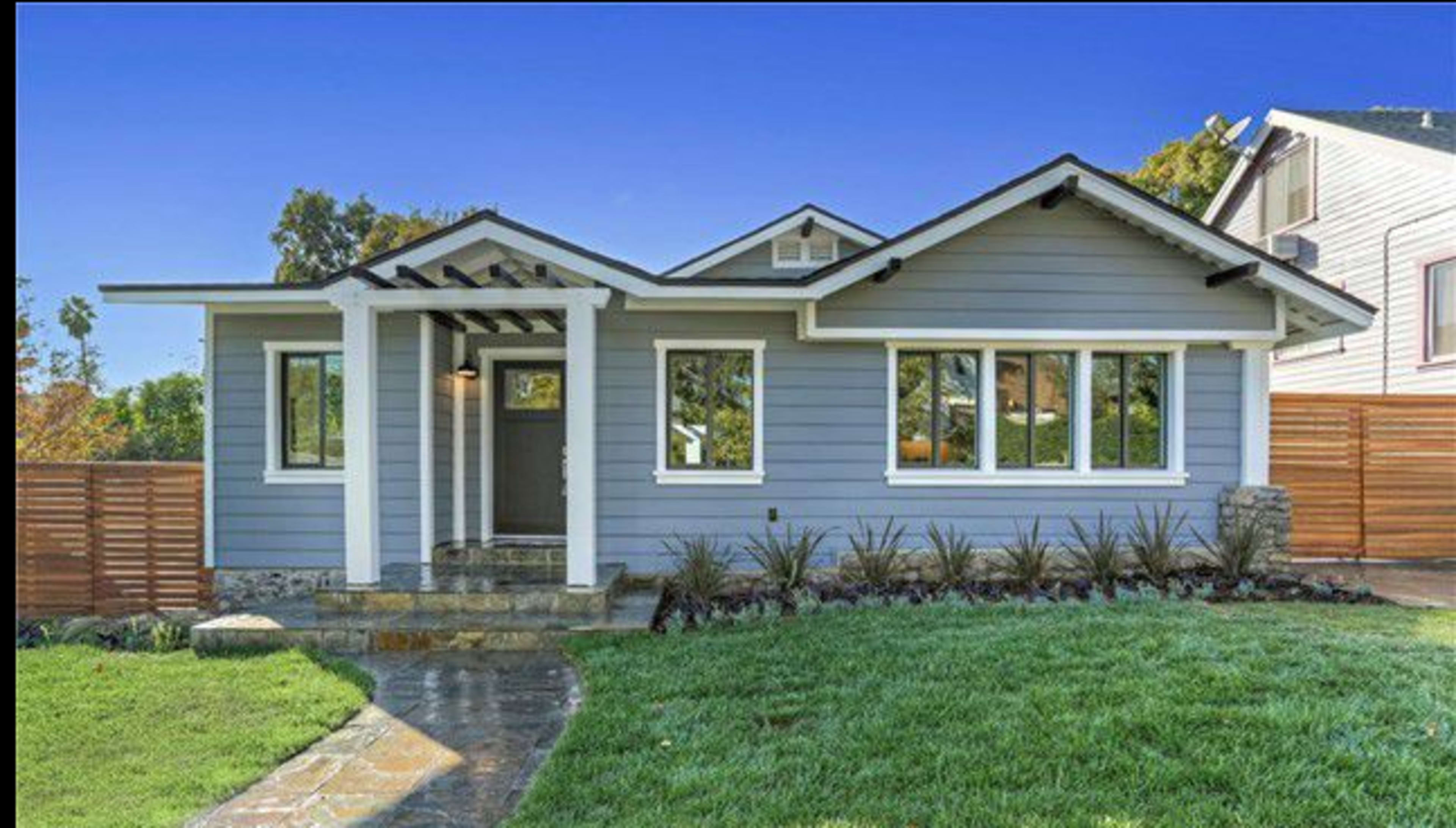 A single-story blue house with a stone pathway, a well-manicured lawn, and wooden fencing.