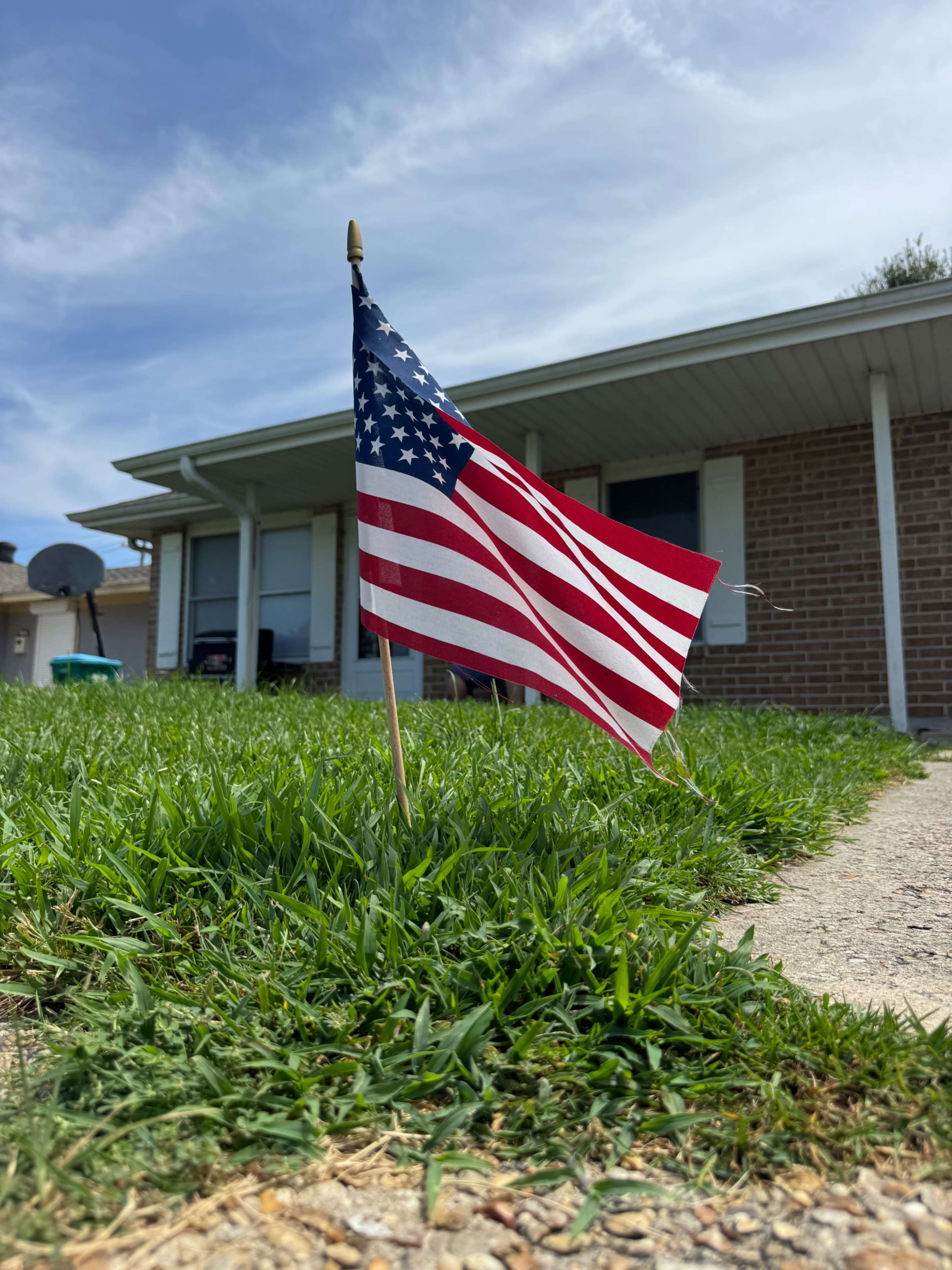 A small American flag is planted in the green grass in front of a house.