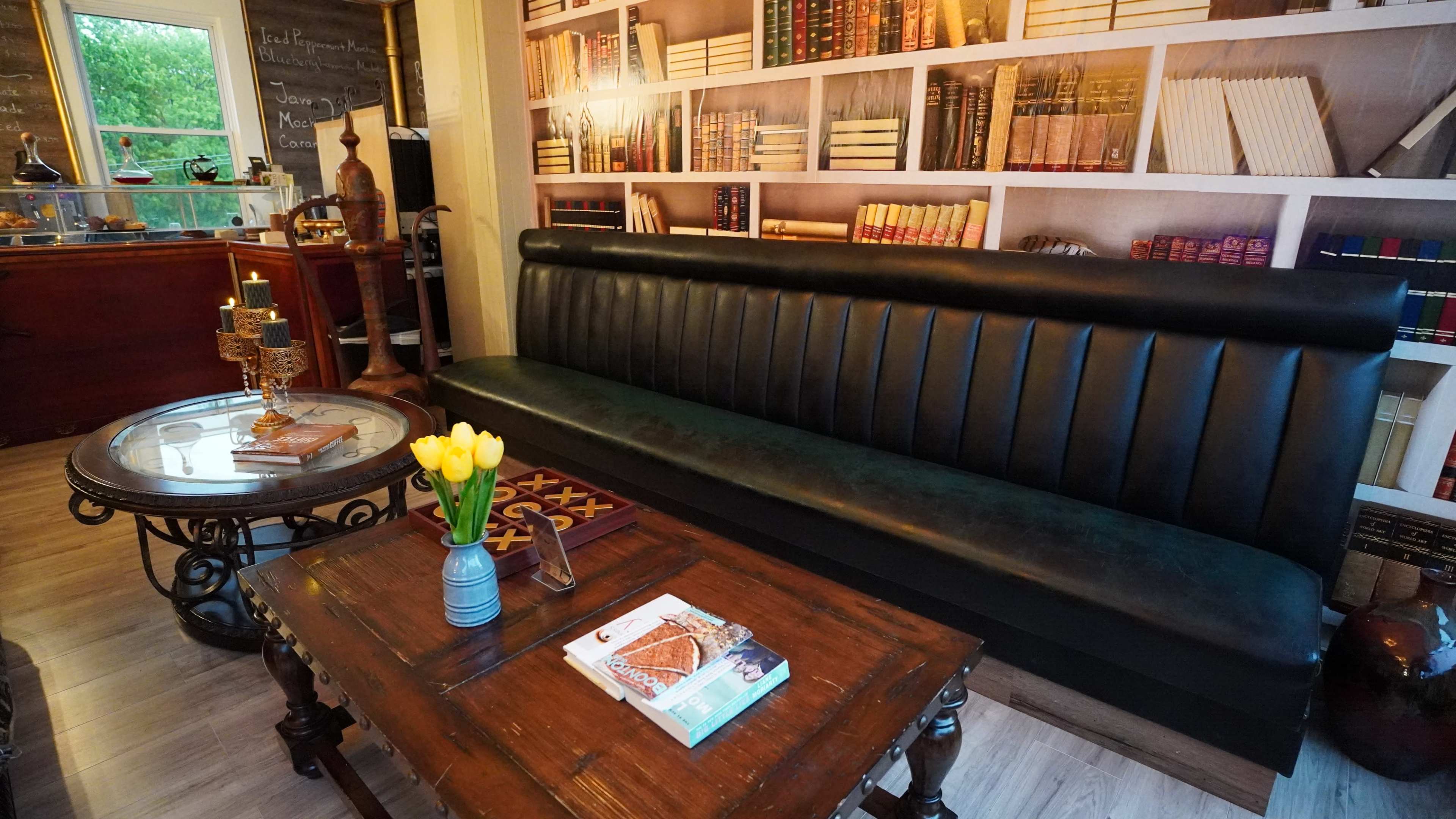 A cozy seating area with a black leather sofa, a wooden table, and a wall featuring bookshelves filled with books.