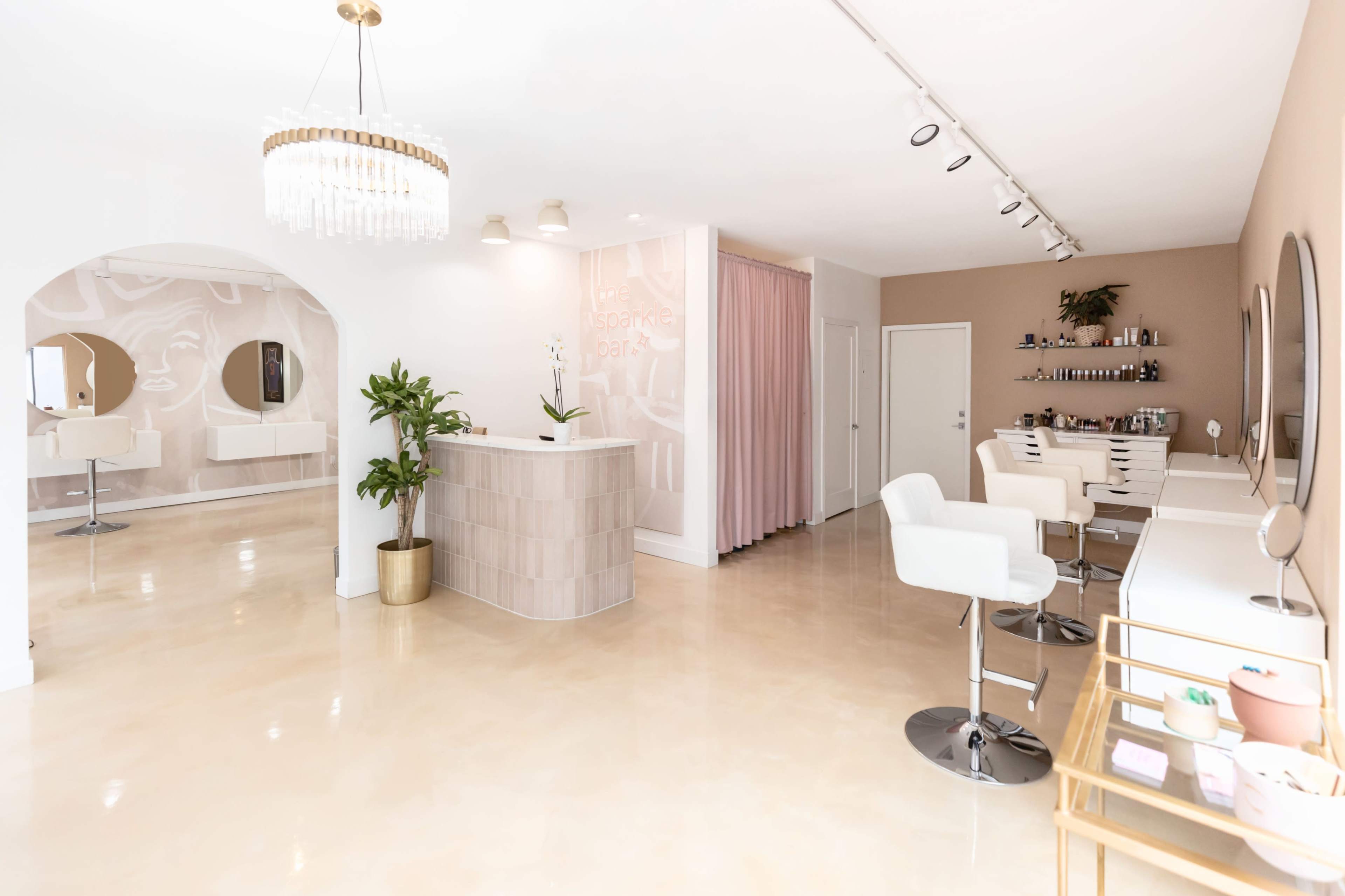 A modern beauty salon interior featuring a reception desk, styling stations, and decorative elements in neutral tones.