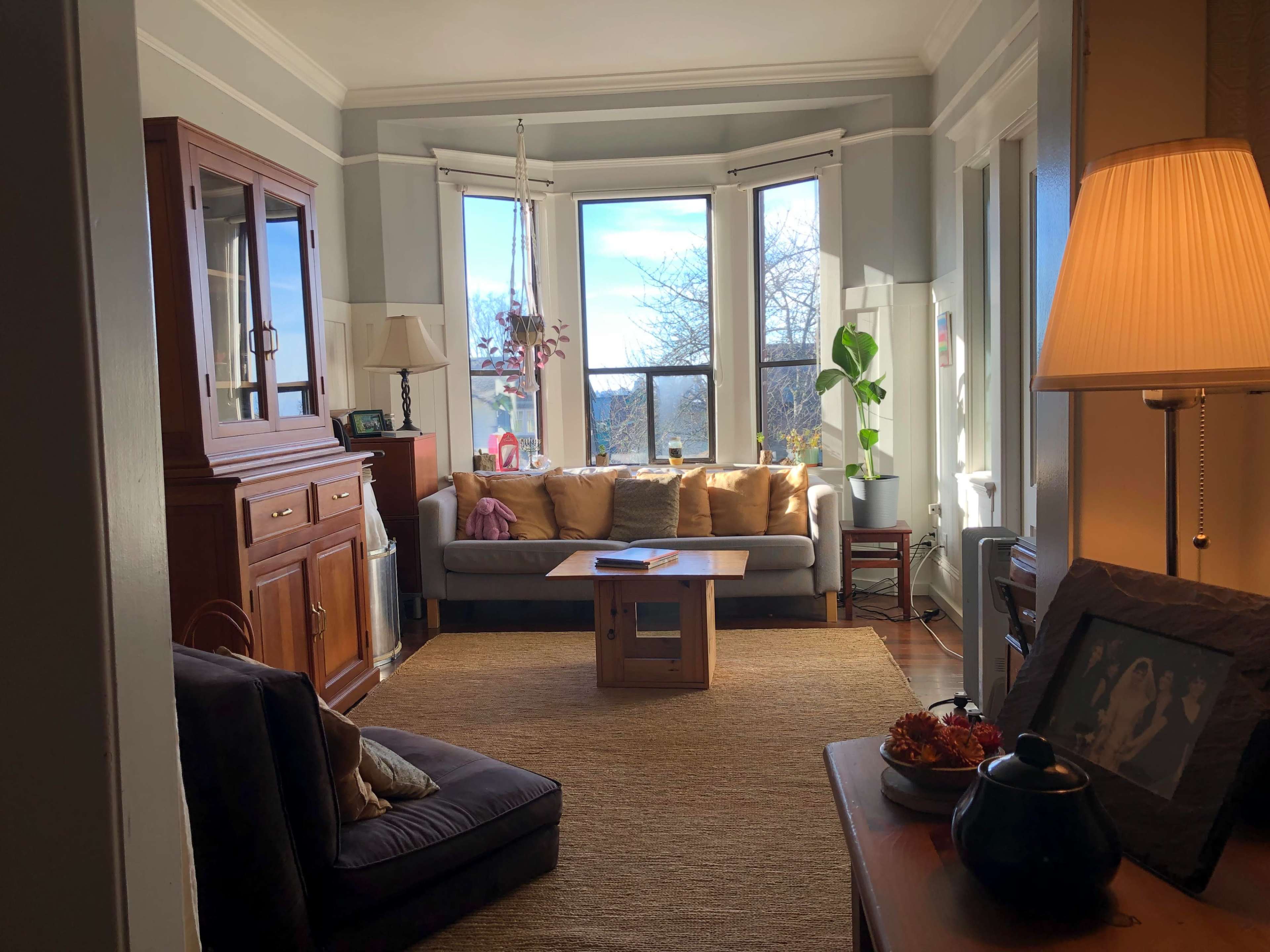 A cozy living room with a sofa, a coffee table in the center, and large windows allowing natural light to enter.