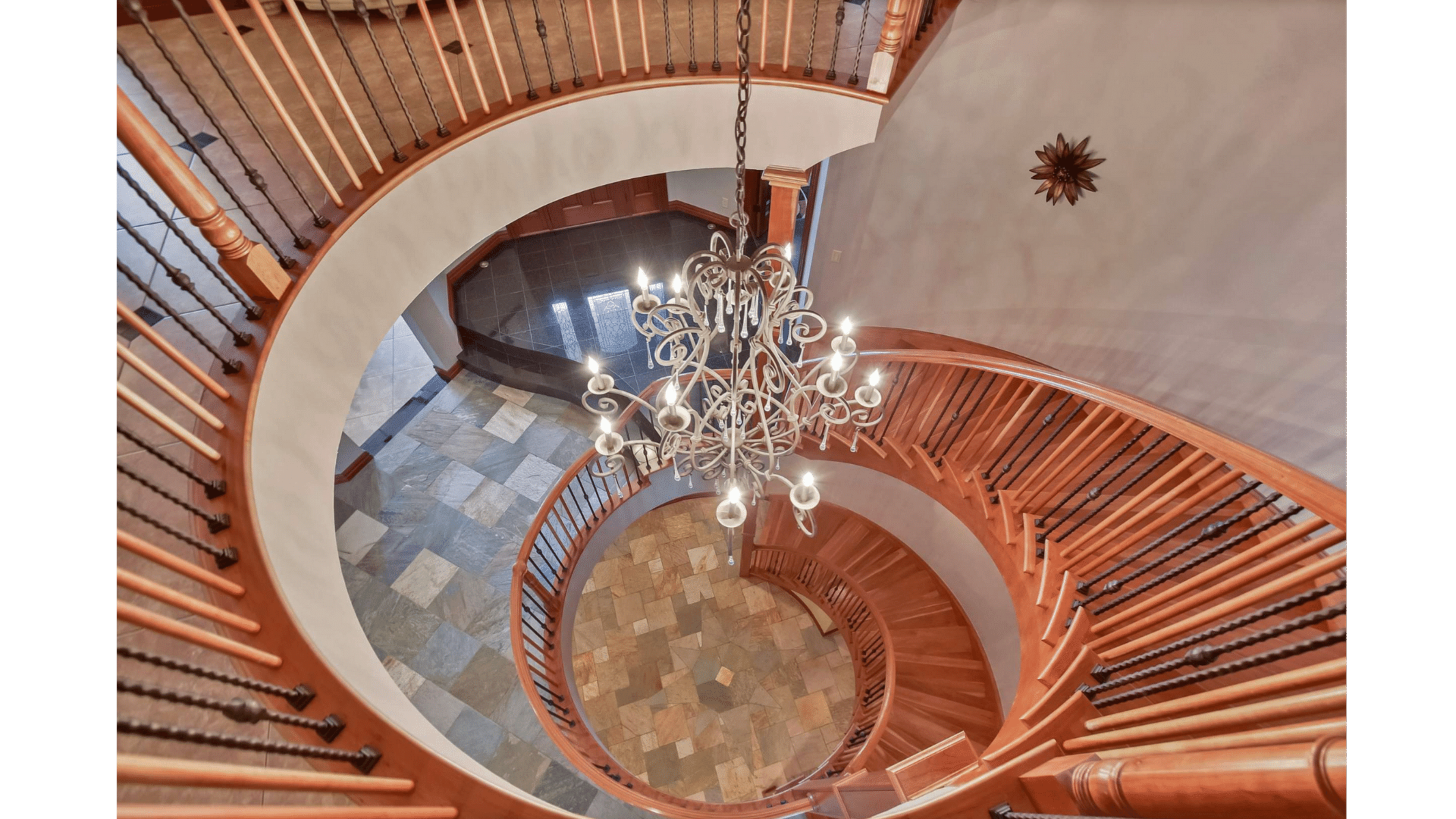 A spiral staircase with wooden railings and a chandelier hanging from the ceiling above.