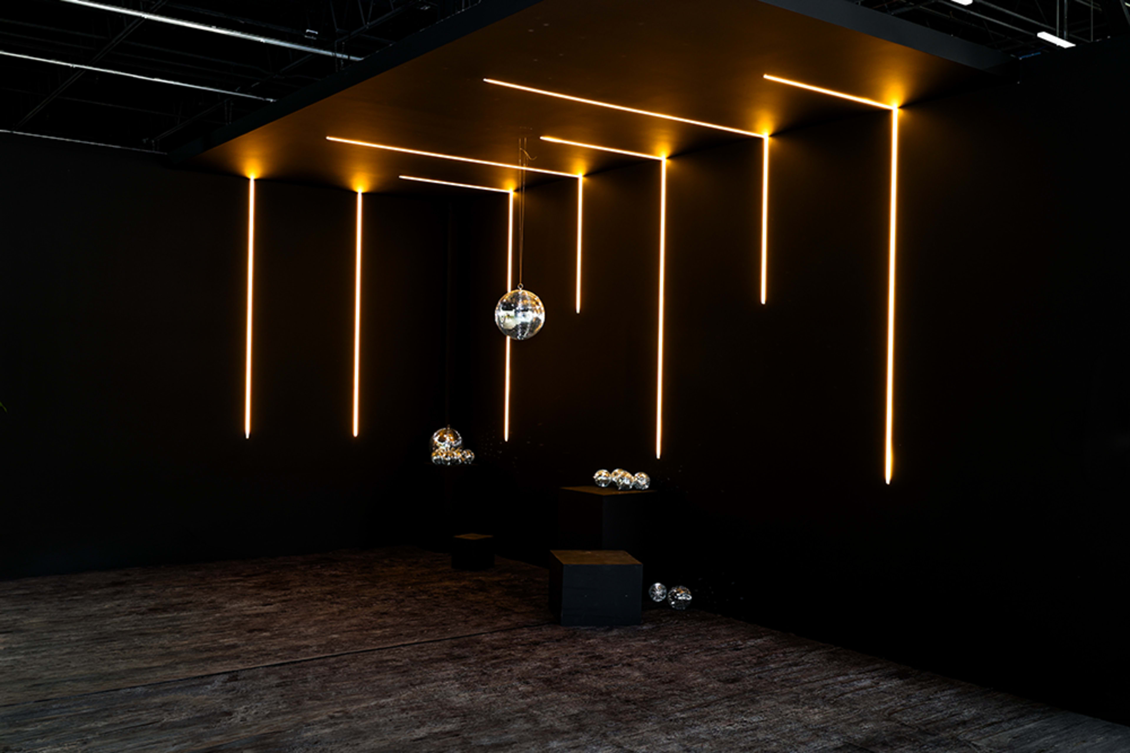 The image shows a dimly lit room with vertical light strips on a black wall and several reflective spheres placed on a dark platform.