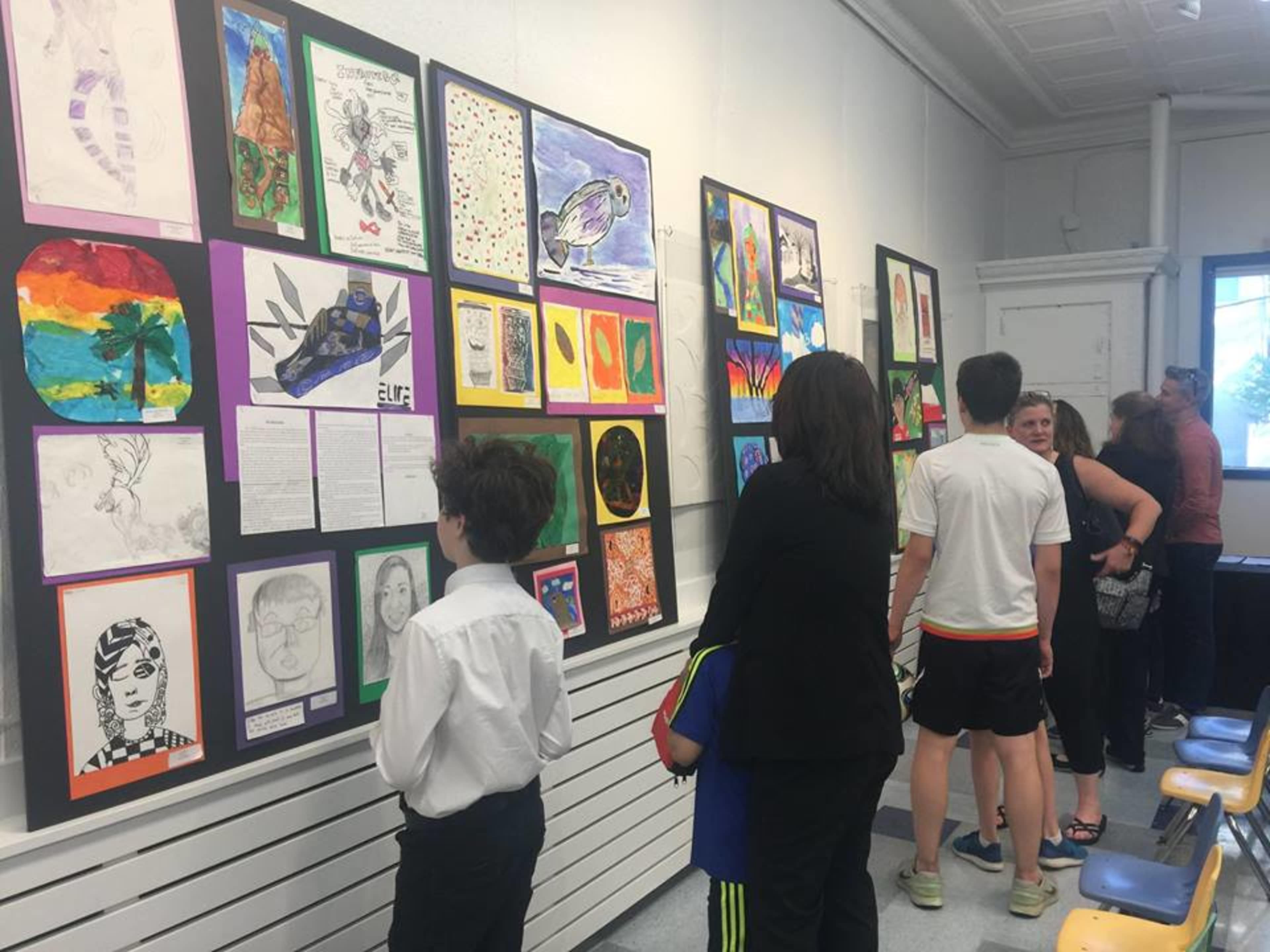 A group of people views artwork displayed on the walls of a school hallway during an exhibition.