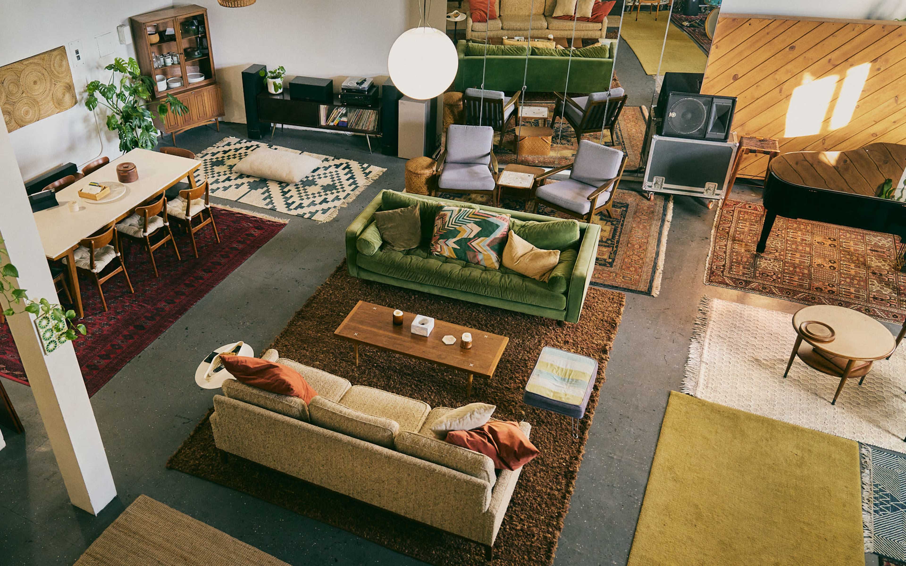 The image features a spacious, stylish living area with multiple seating options, a large dining table, and various patterned rugs on the floor.
