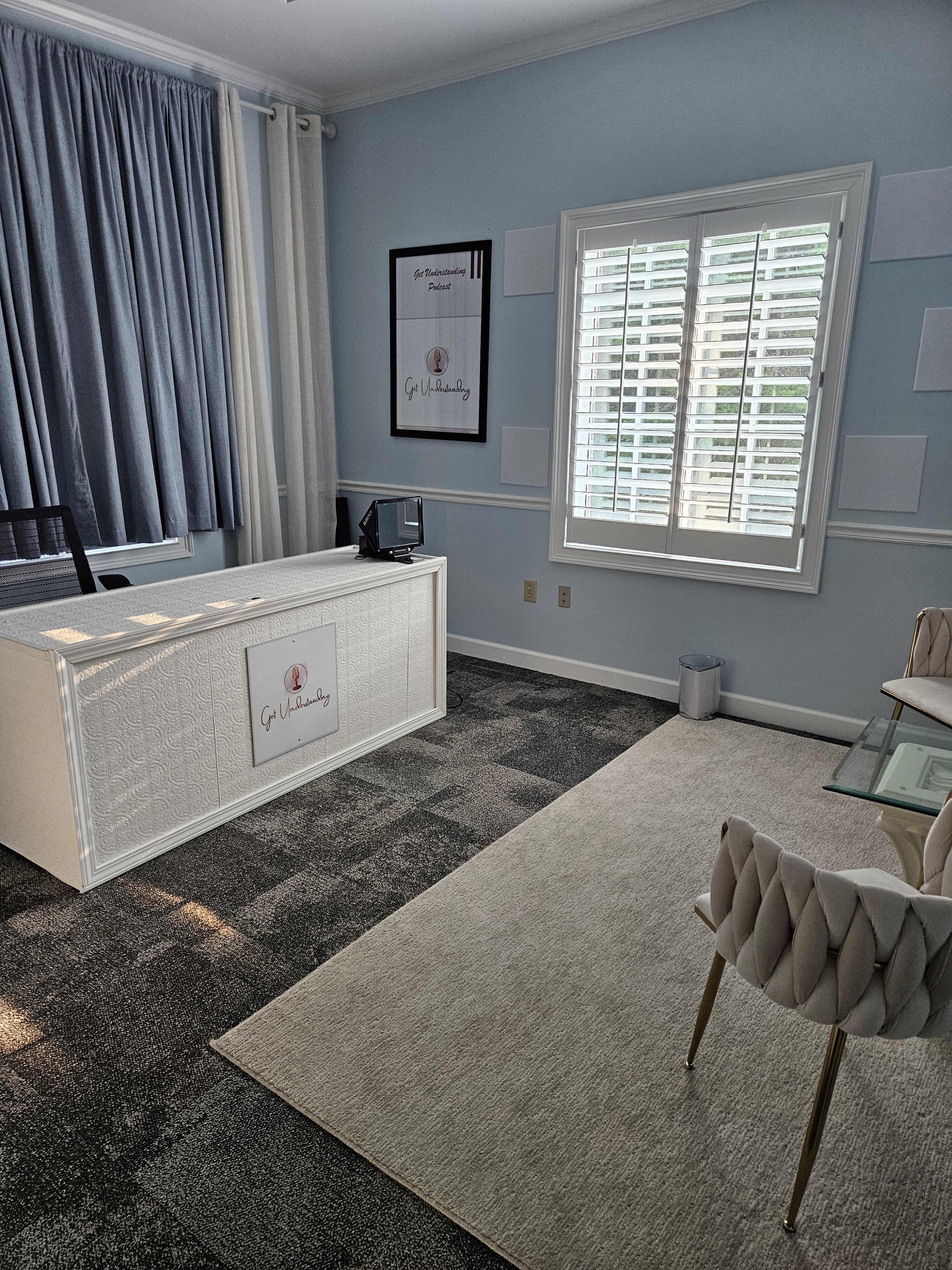 The image depicts a modern office reception area with a white front desk, a light-colored rug, and a large window covered by blue drapes.