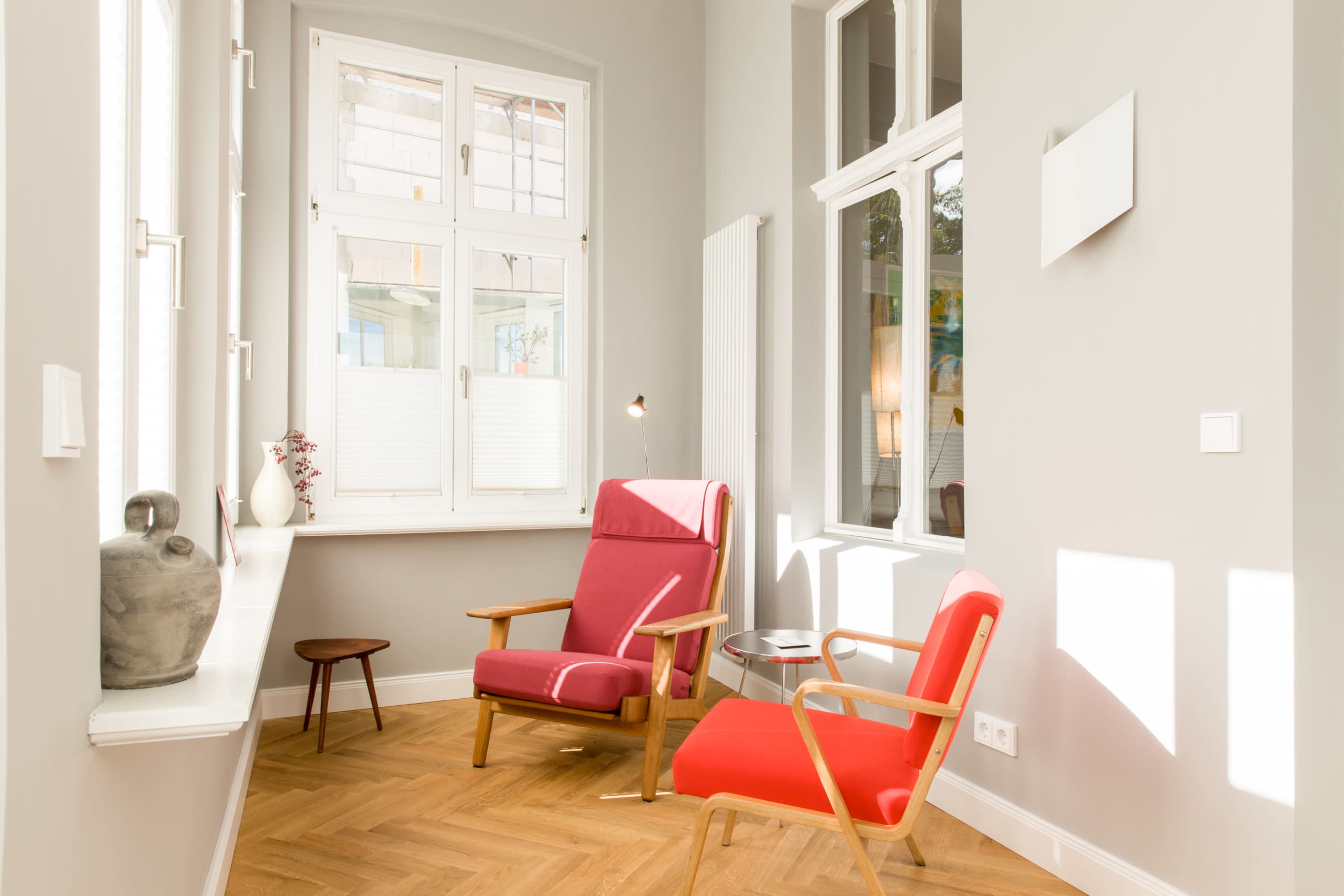 A bright room features two red armchairs and a small round table beside a large window with natural light streaming in.