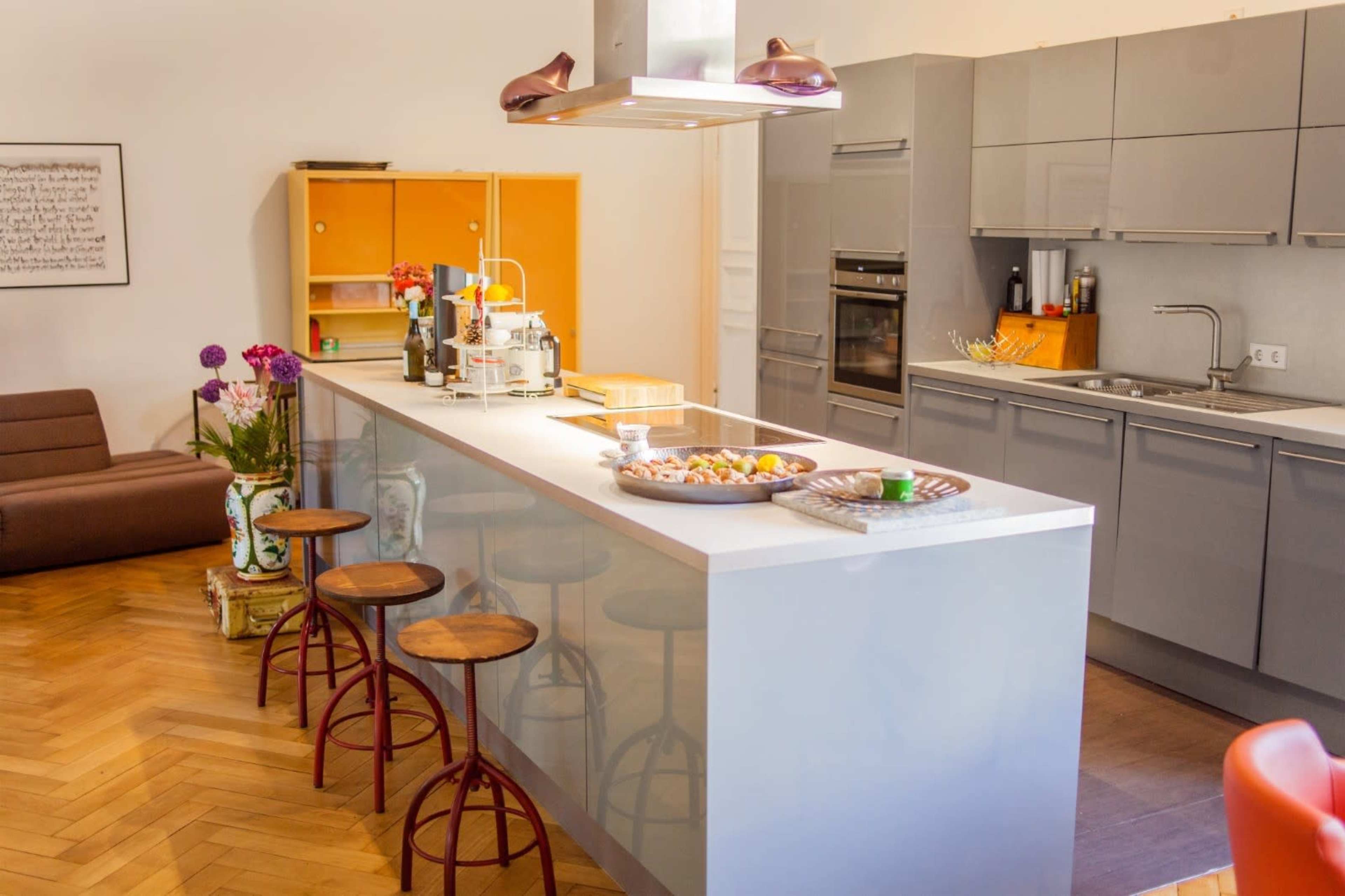 The kitchen features a central island with bar stools, modern gray cabinets, and wooden flooring.