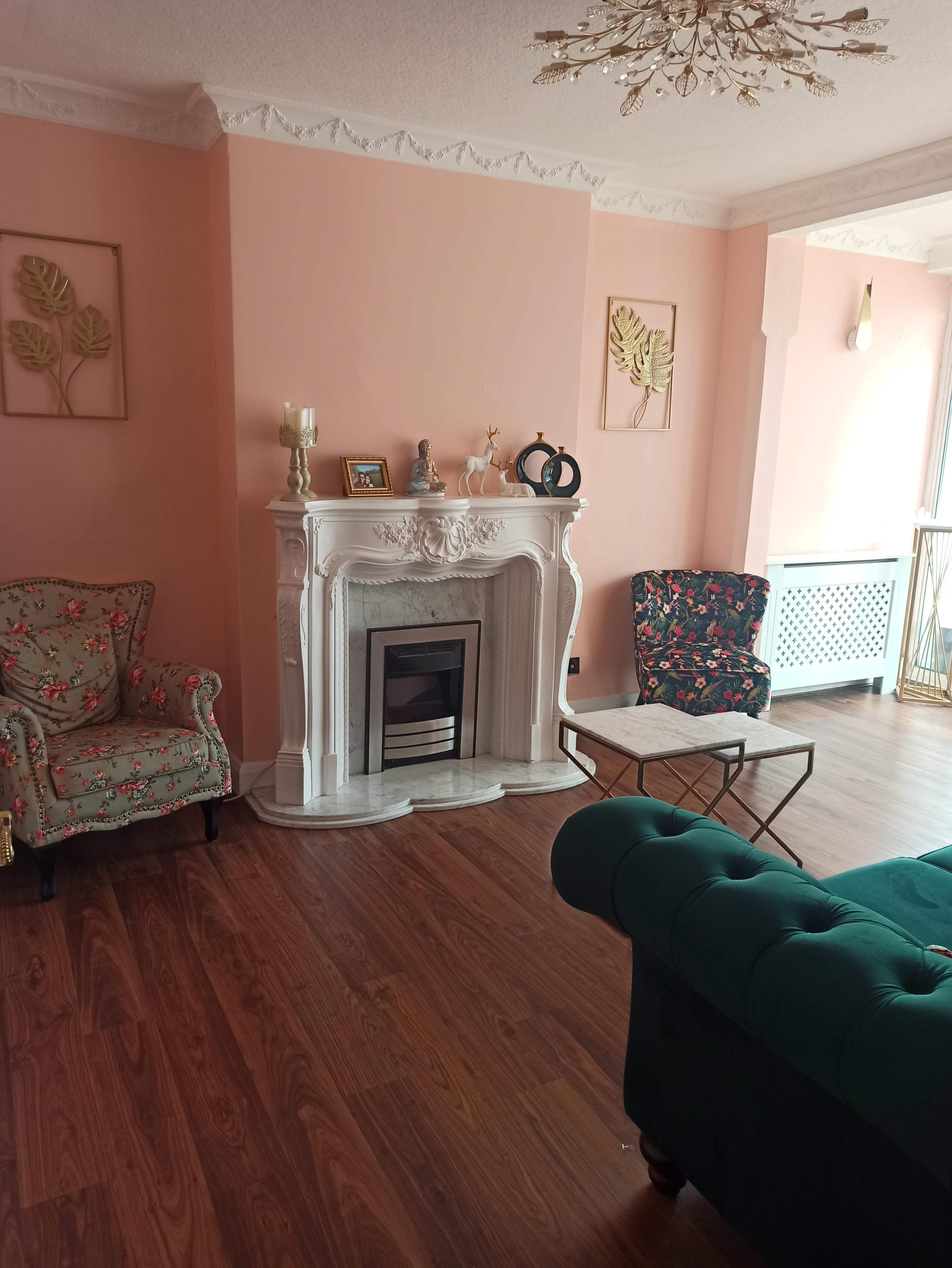 A living room with a pink wall, a decorative fireplace, a patterned armchair, and a small coffee table.