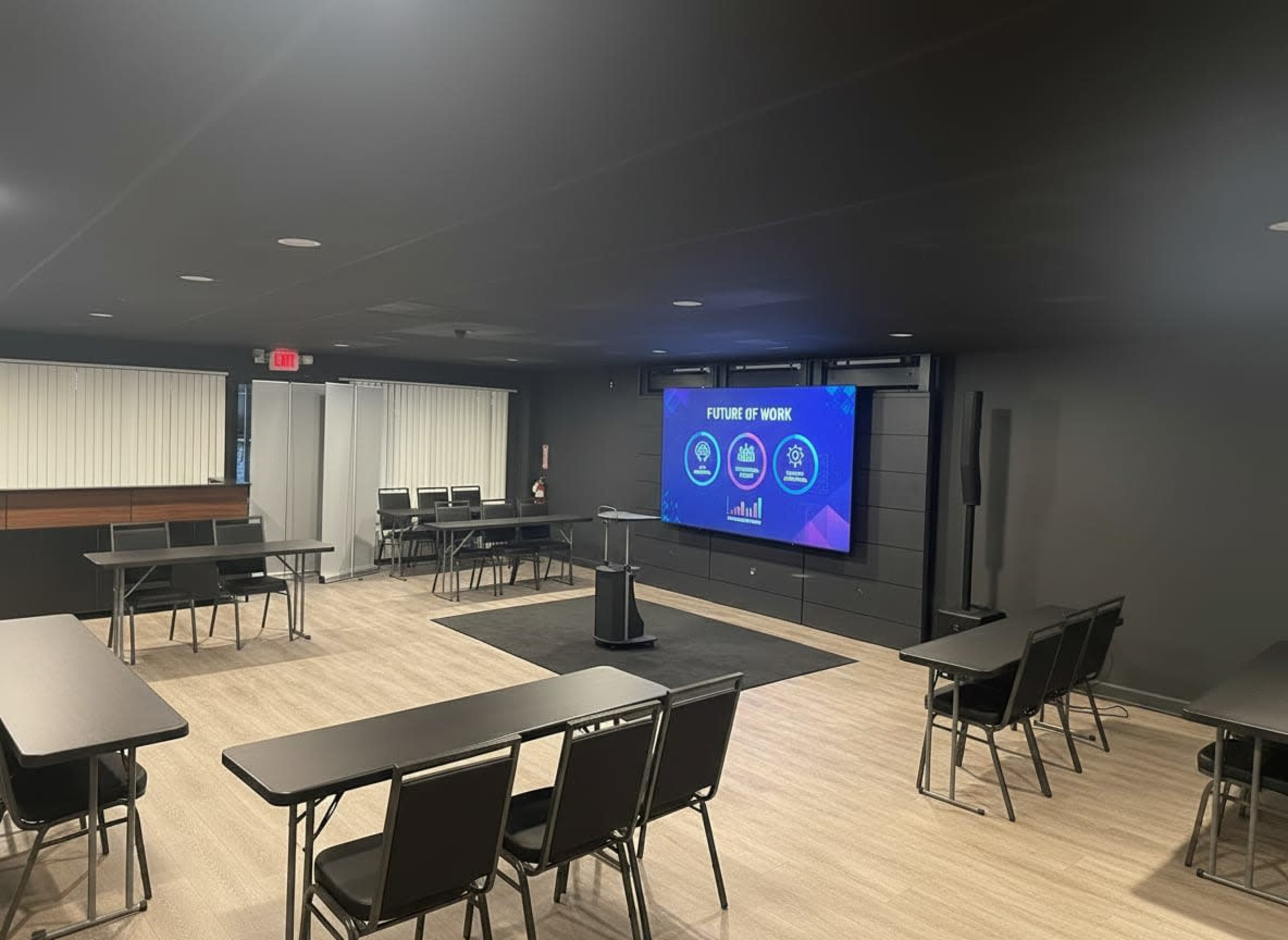 A modern conference room is set up with rows of chairs and tables facing a large screen displaying "FUTURE OF WORK."