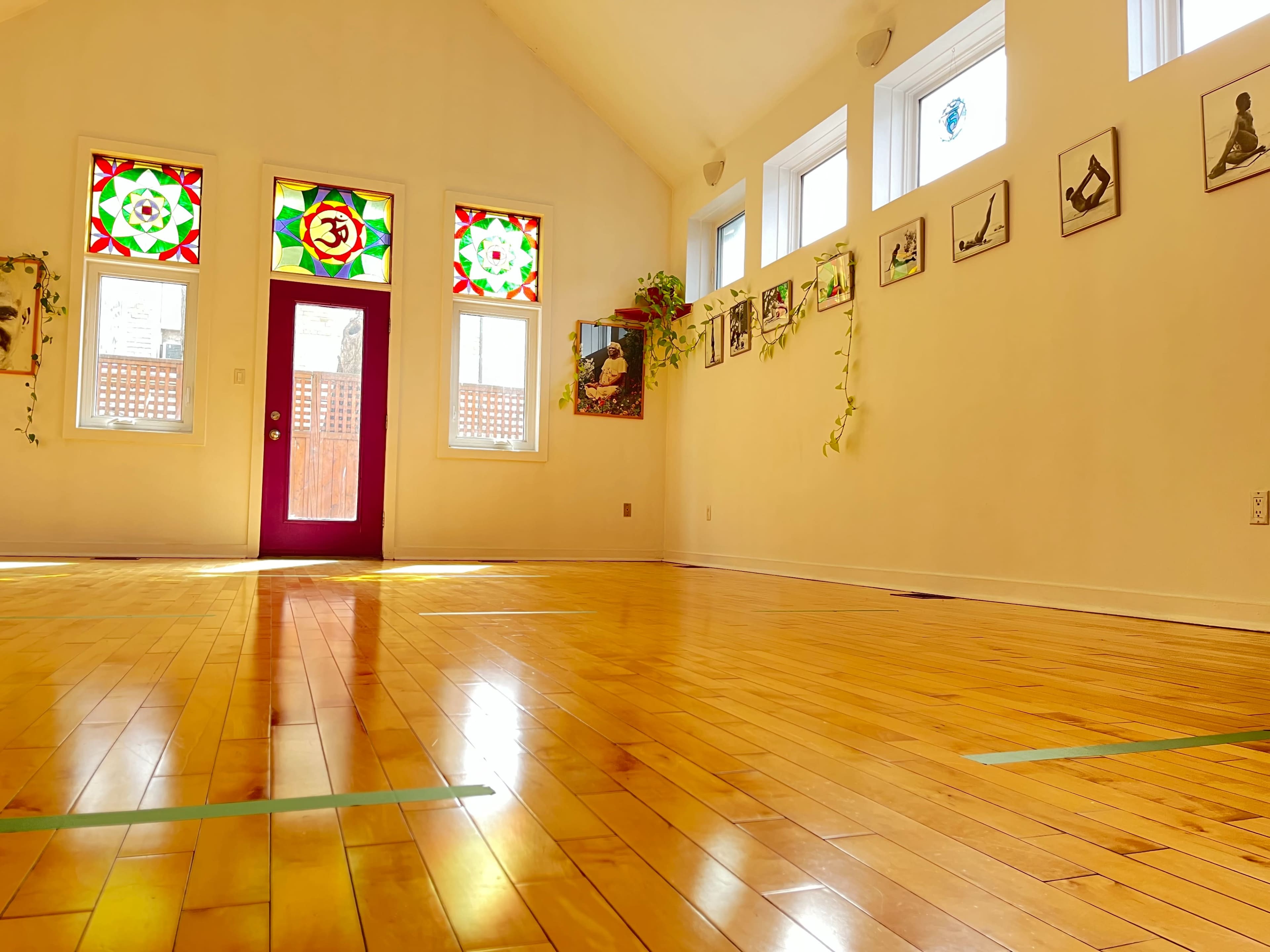 A spacious, well-lit room with wooden flooring, colorful stained glass windows, and framed images on the walls.