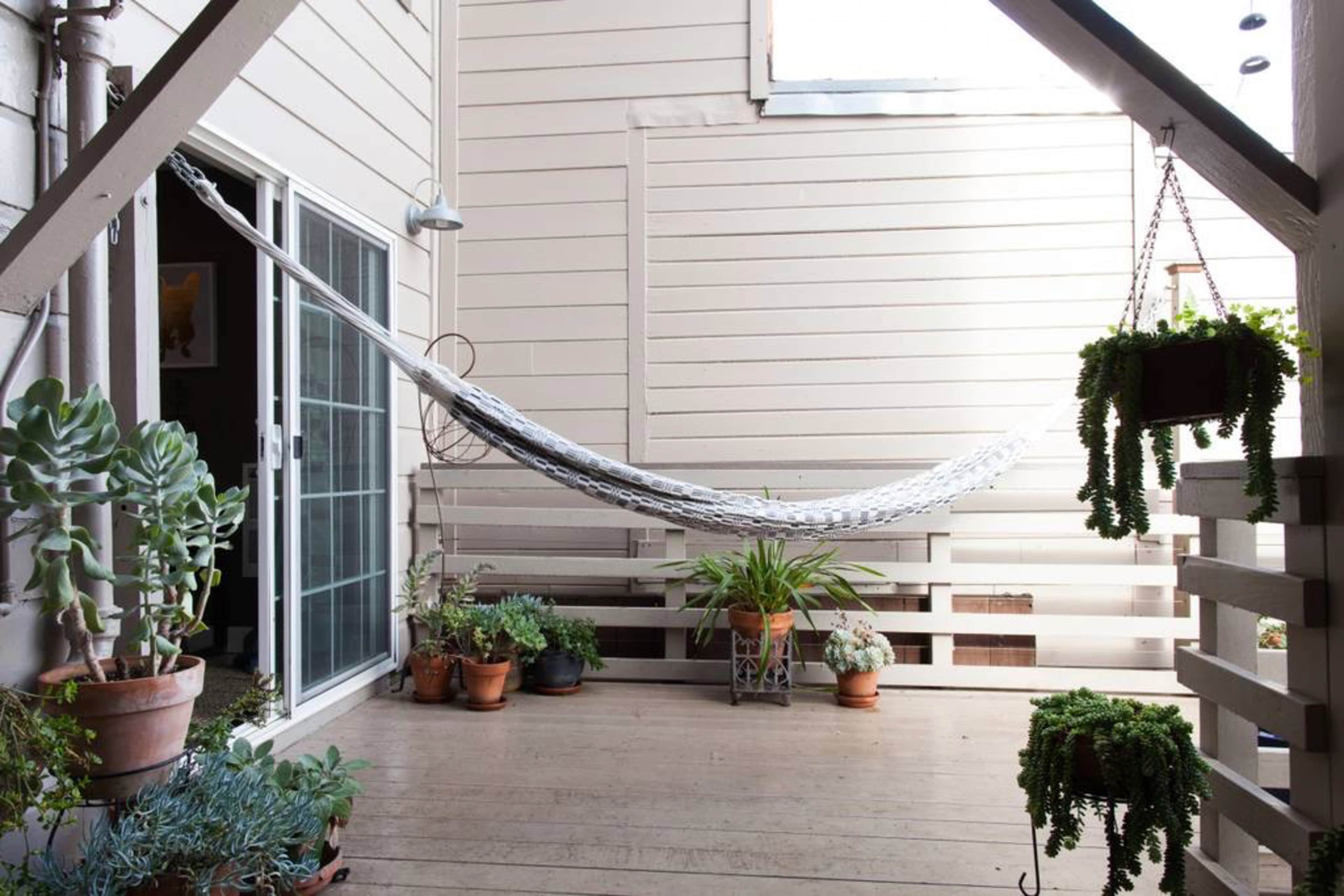 A hammock is suspended between wooden beams on a patio surrounded by potted plants.