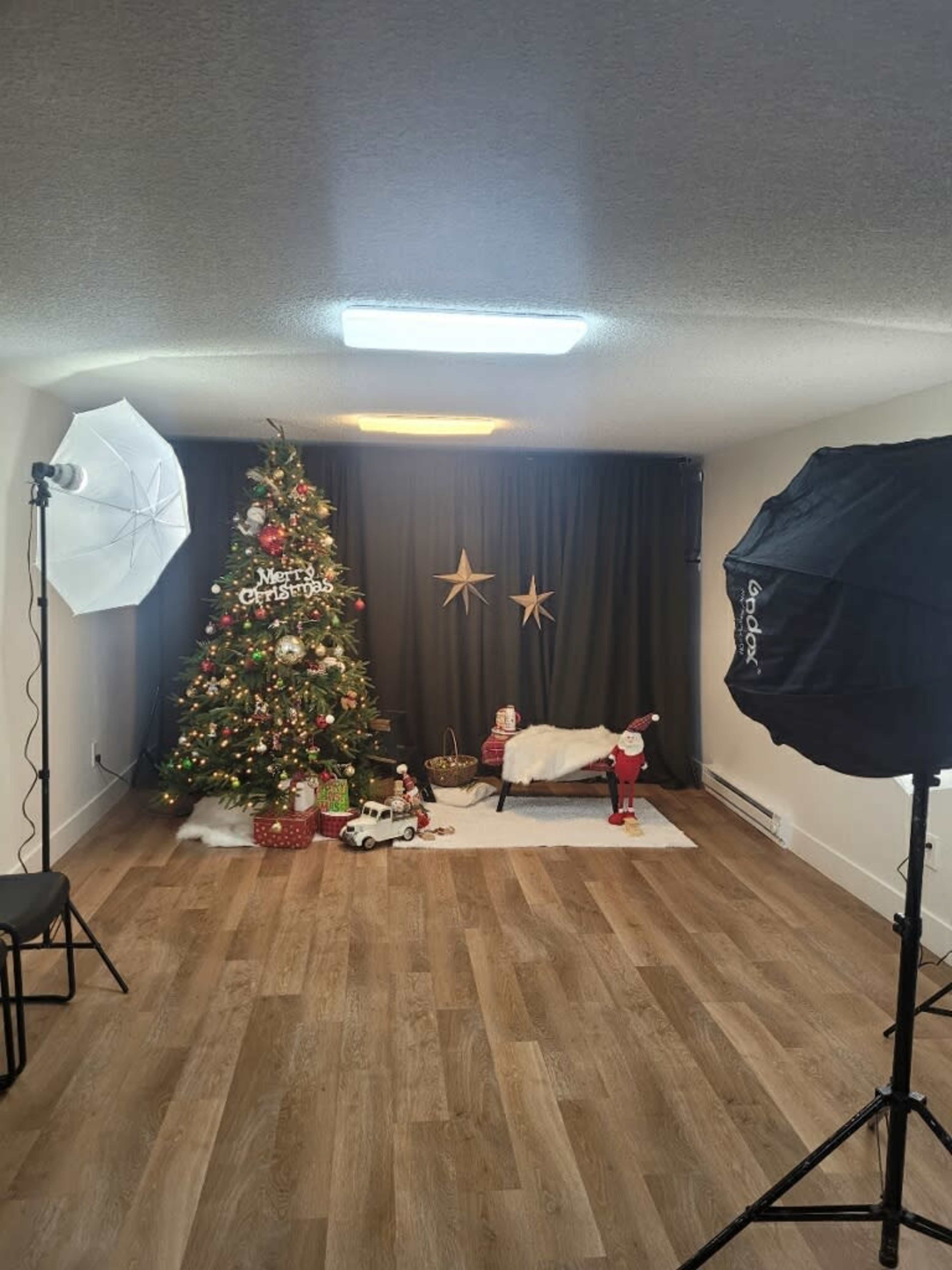 The image shows a decorated Christmas set featuring a Christmas tree, a bed with a blanket, and holiday props, enhanced by studio lighting.