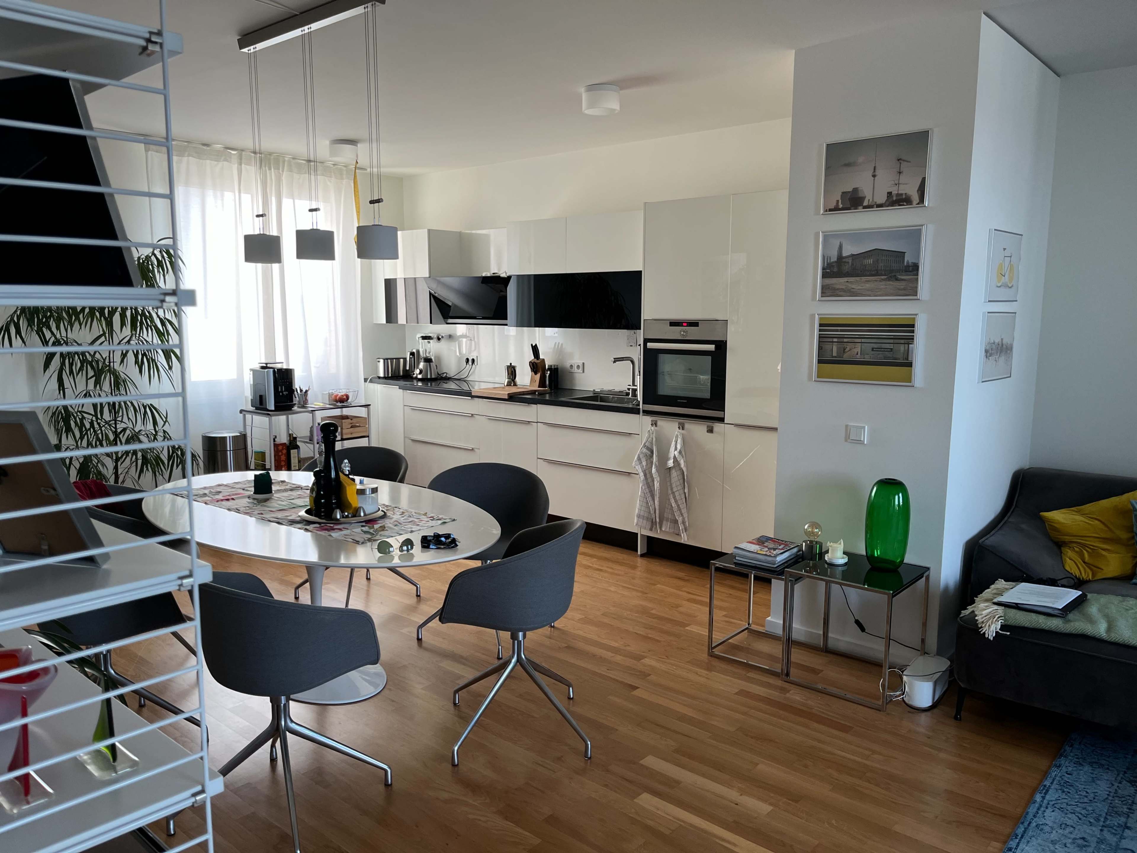The image shows a modern kitchen and dining area with a circular table, four chairs, and sleek white cabinetry.