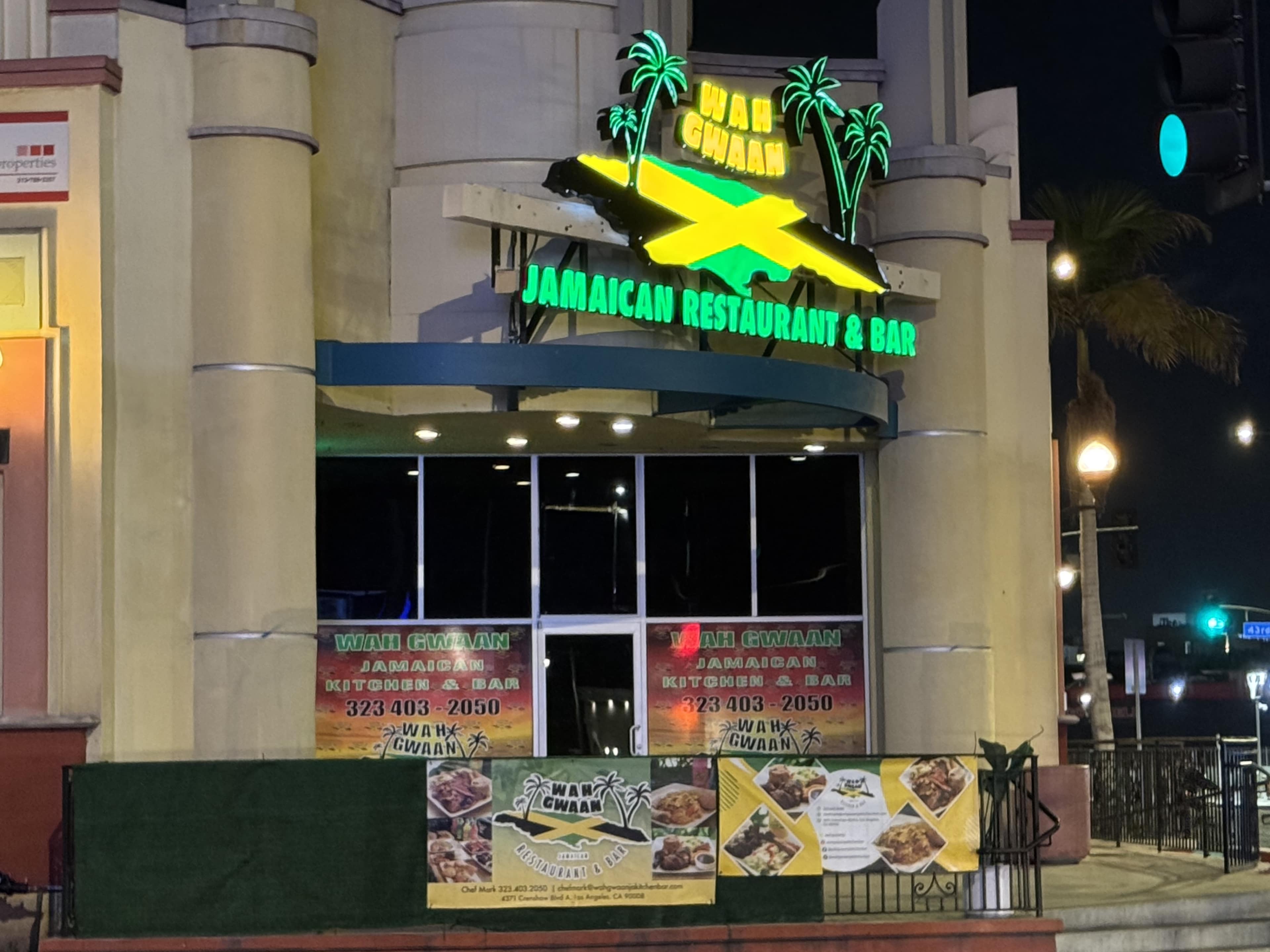 The image shows a Jamaican restaurant and bar with neon signage and promotional banners displayed outside.