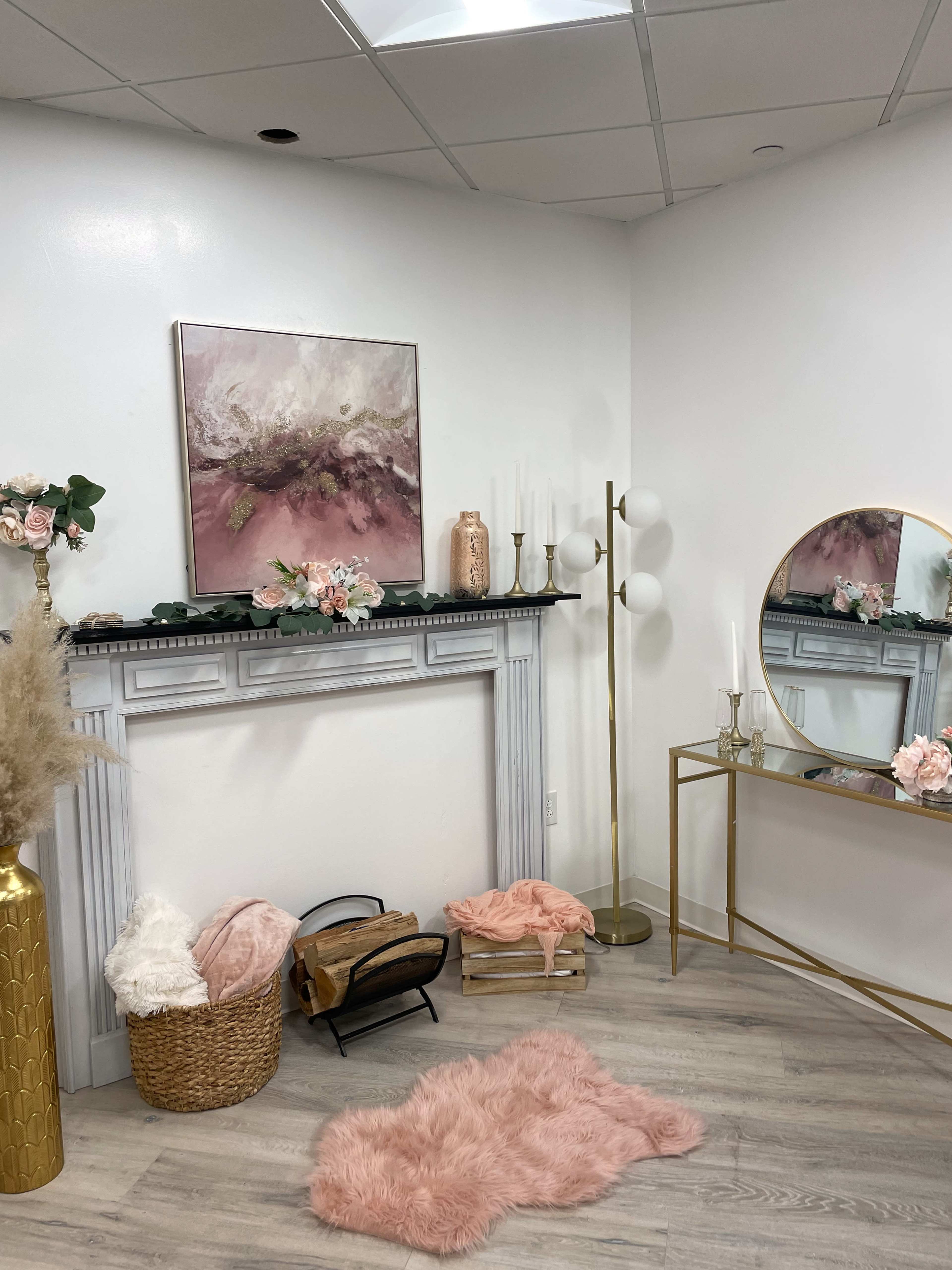 A softly decorated indoor setting featuring a faux fireplace, a mirror, a gold side table, and a plush area rug.