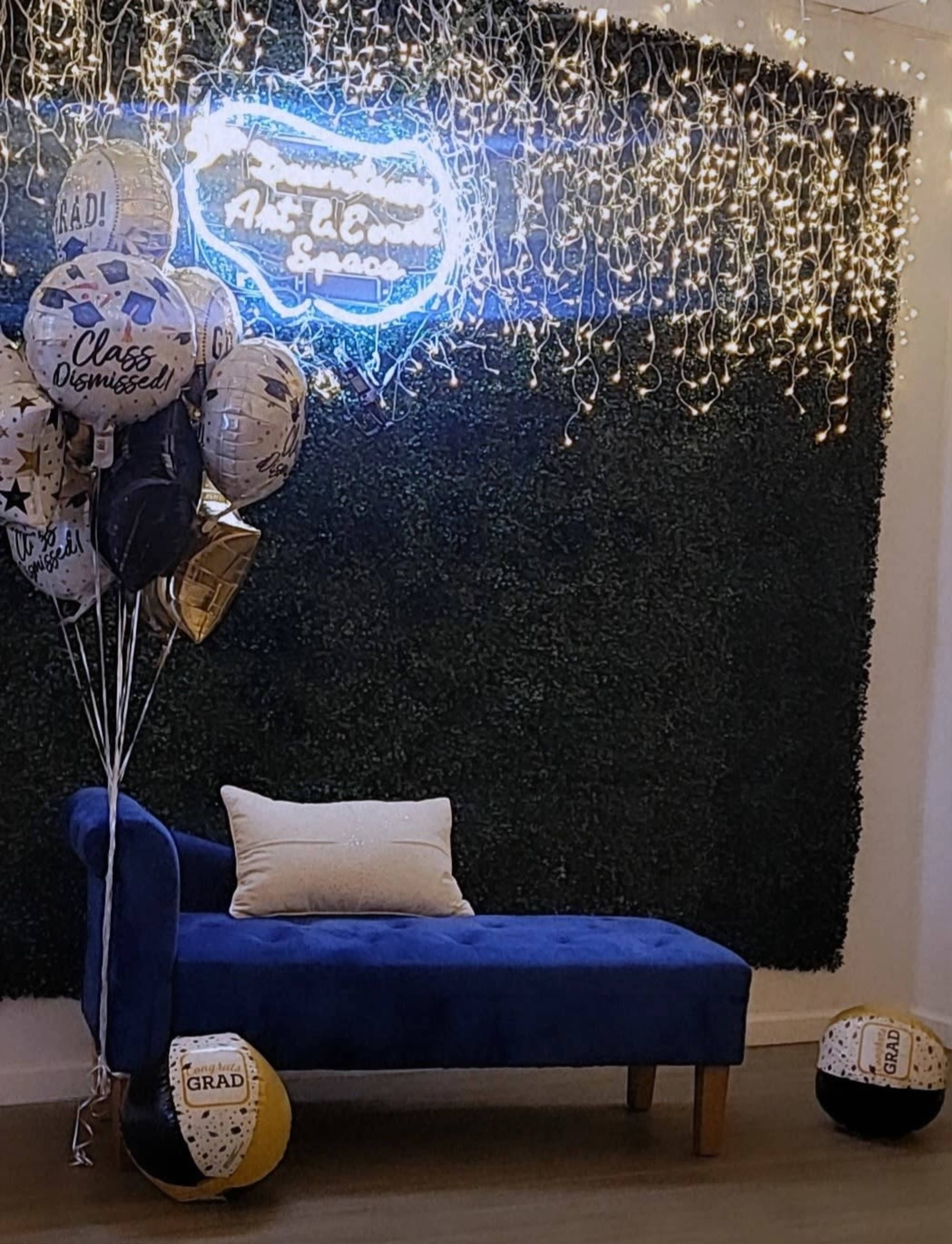 A blue couch against a green wall decorated with fairy lights and balloons celebrating graduation.