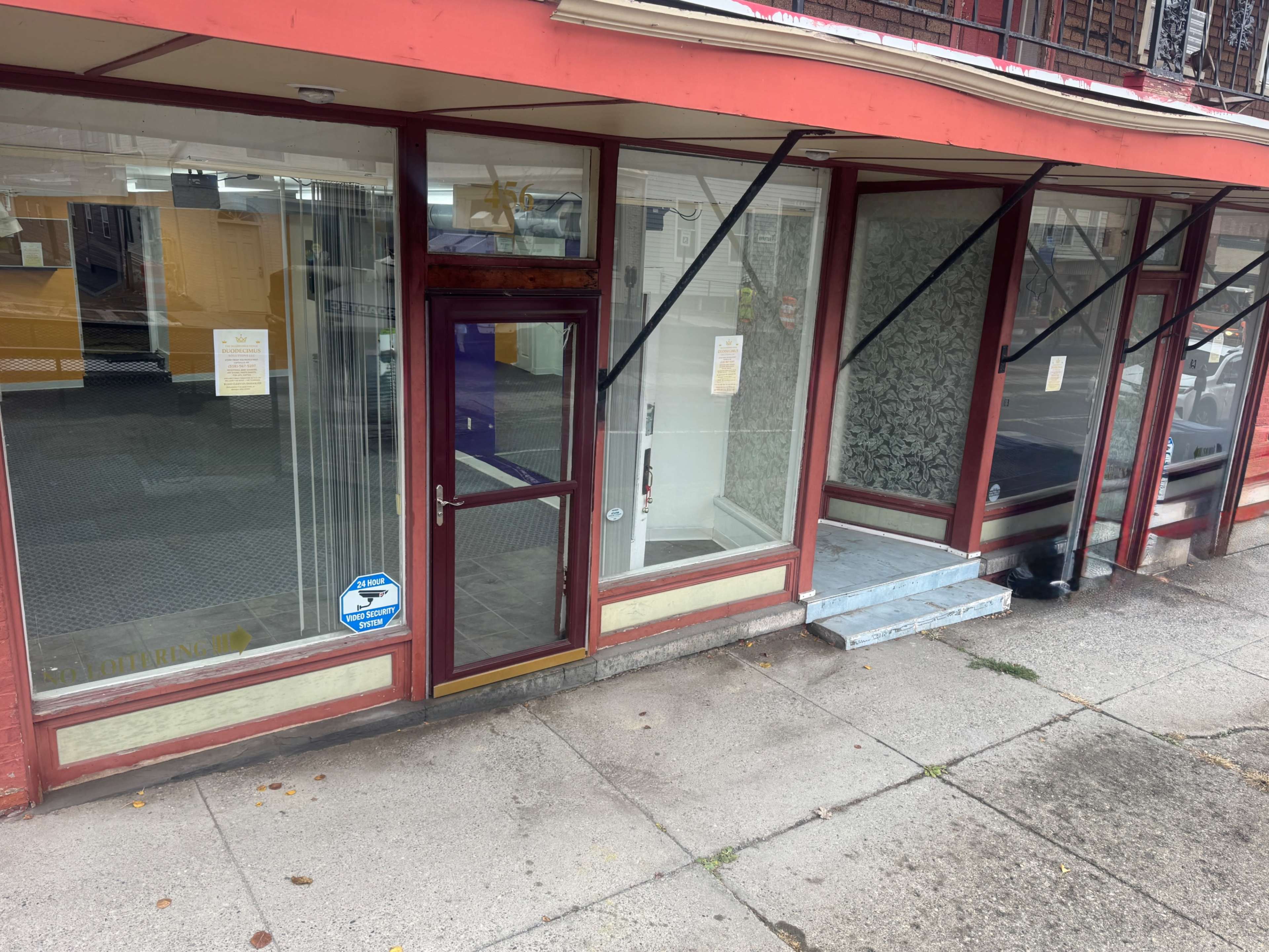 The image shows a storefront with large windows, a glass door, and a set of stairs leading up to a higher entrance.