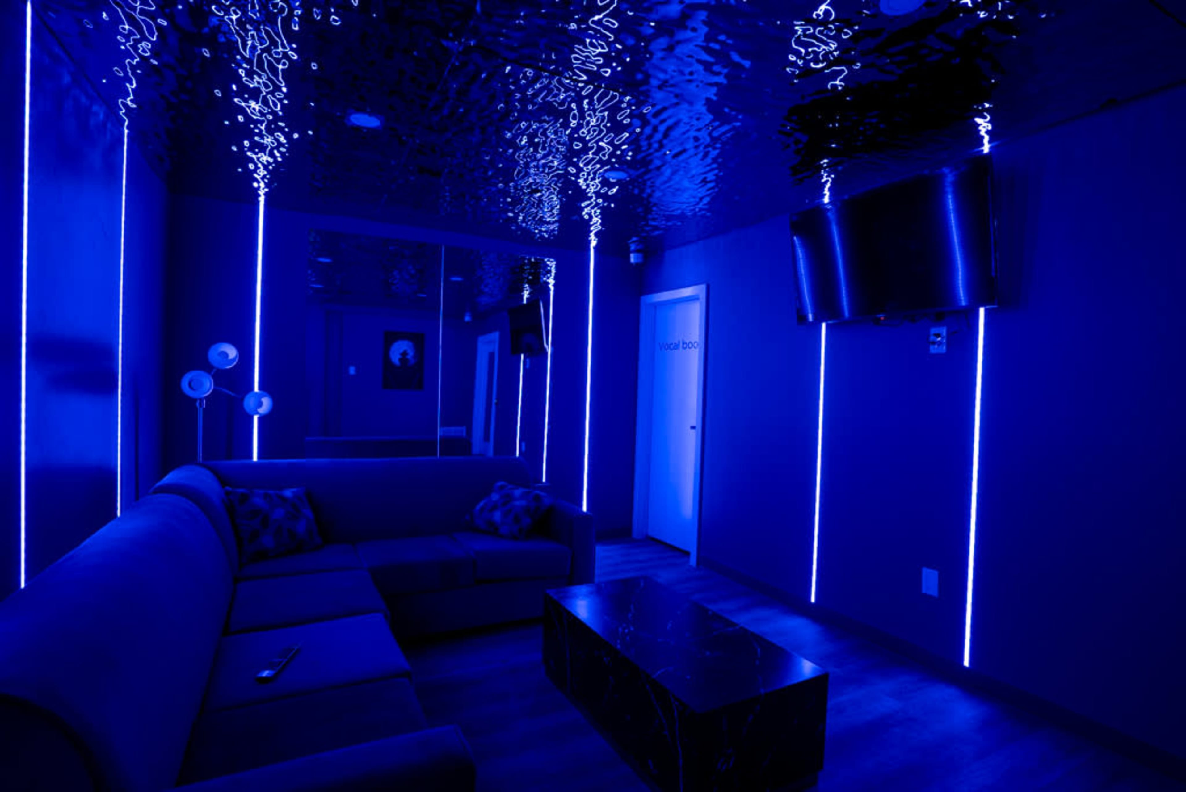 A dimly lit room with blue LED lights, featuring a couch, a coffee table, and a television mounted on the wall.