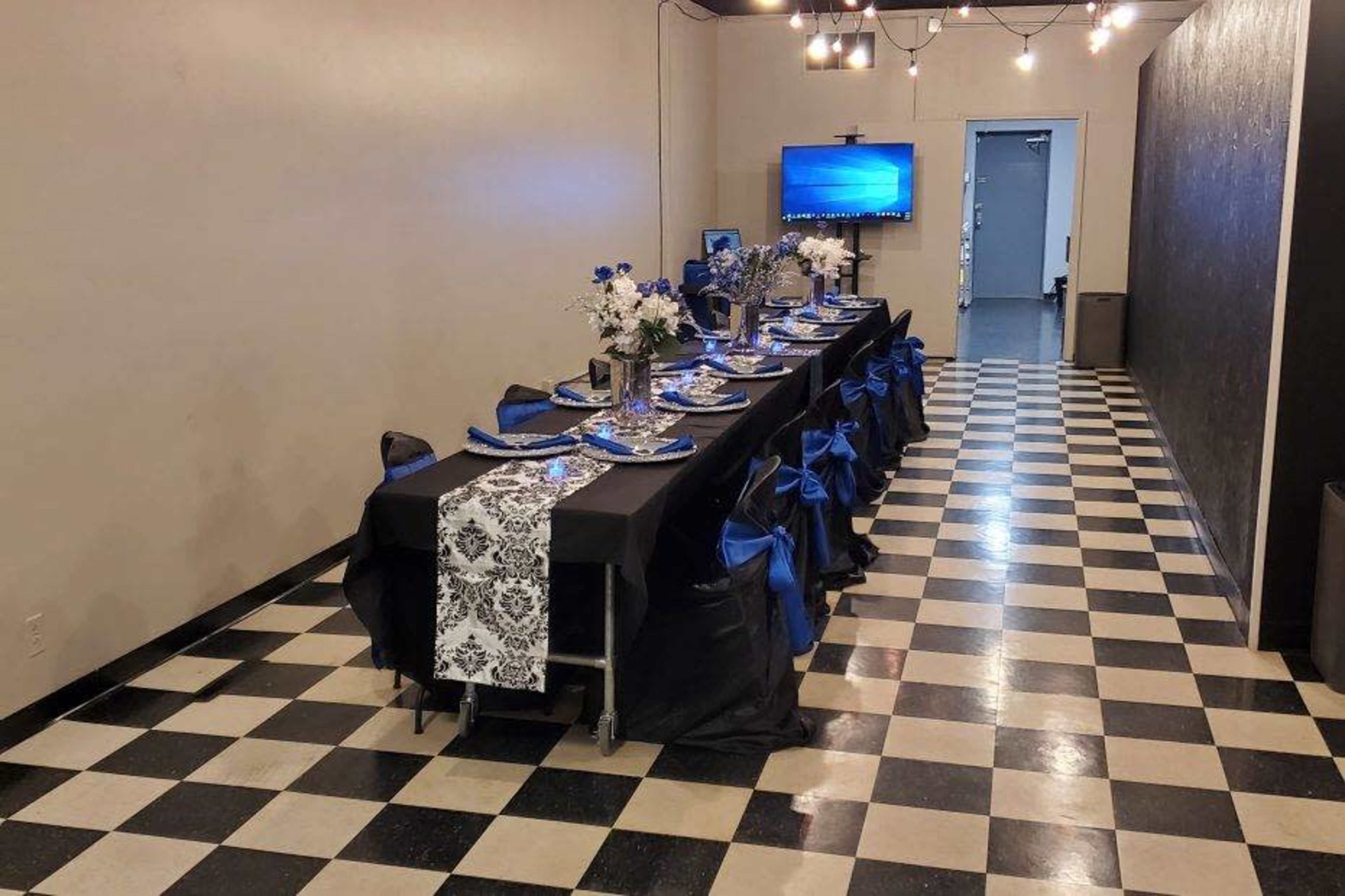 A long dining table is set with blue and silver decorations in a room with black and white checkered flooring.