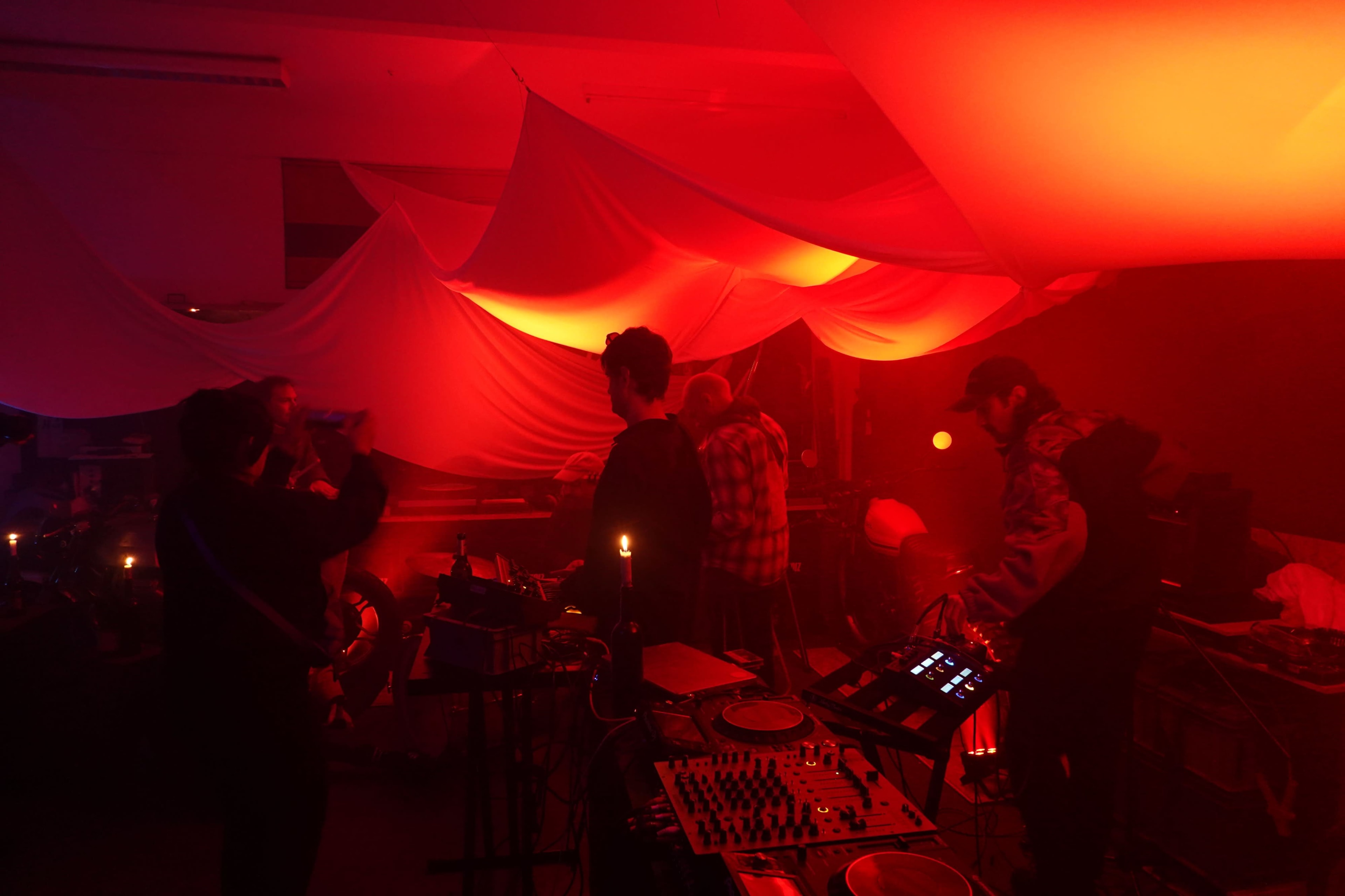 A group of people is gathered in a dimly lit room with red lighting, engaged in music production and performance.