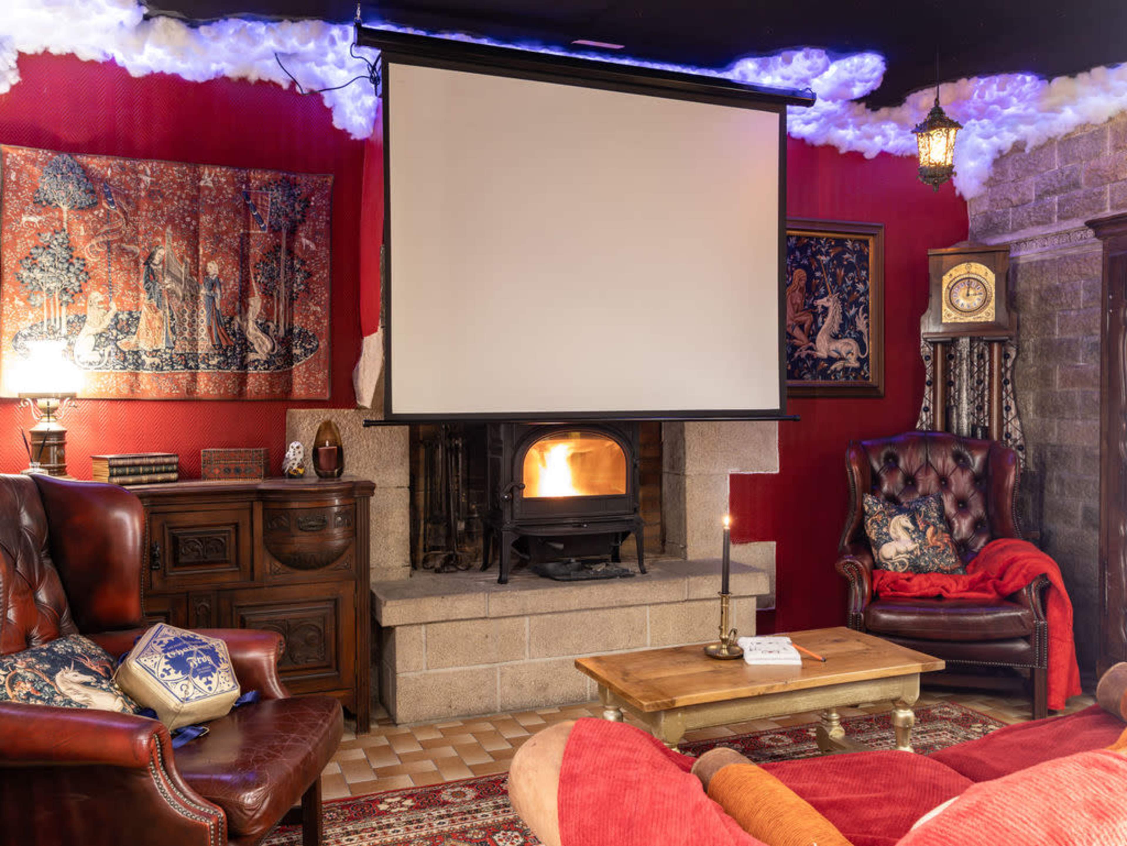 The image shows a cozy living room with a fireplace, a large projection screen, and comfortable seating arranged around a wooden coffee table.