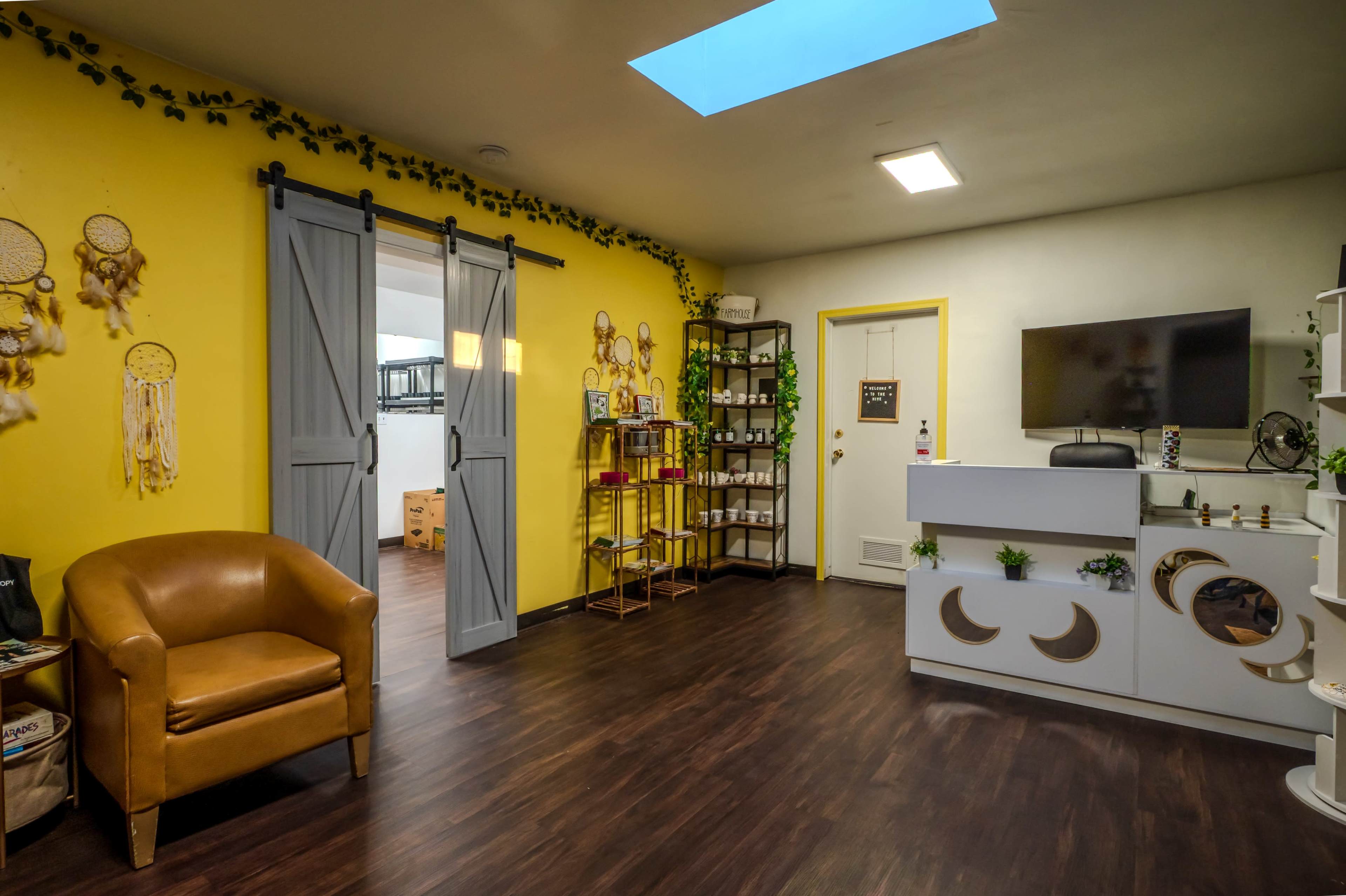 The image shows a brightly painted room with yellow walls, featuring a cozy brown chair, a cabinet with decorative items, and a television mounted on the wall.