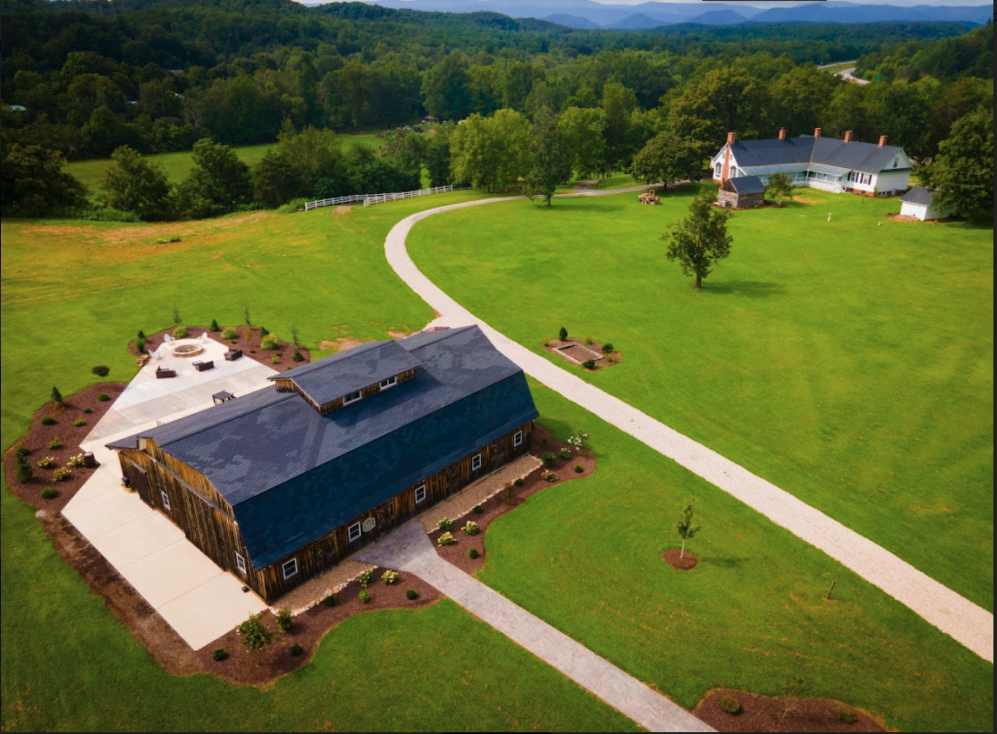 A large, open landscape featuring a barn and a main building surrounded by neatly landscaped grounds and a winding path.