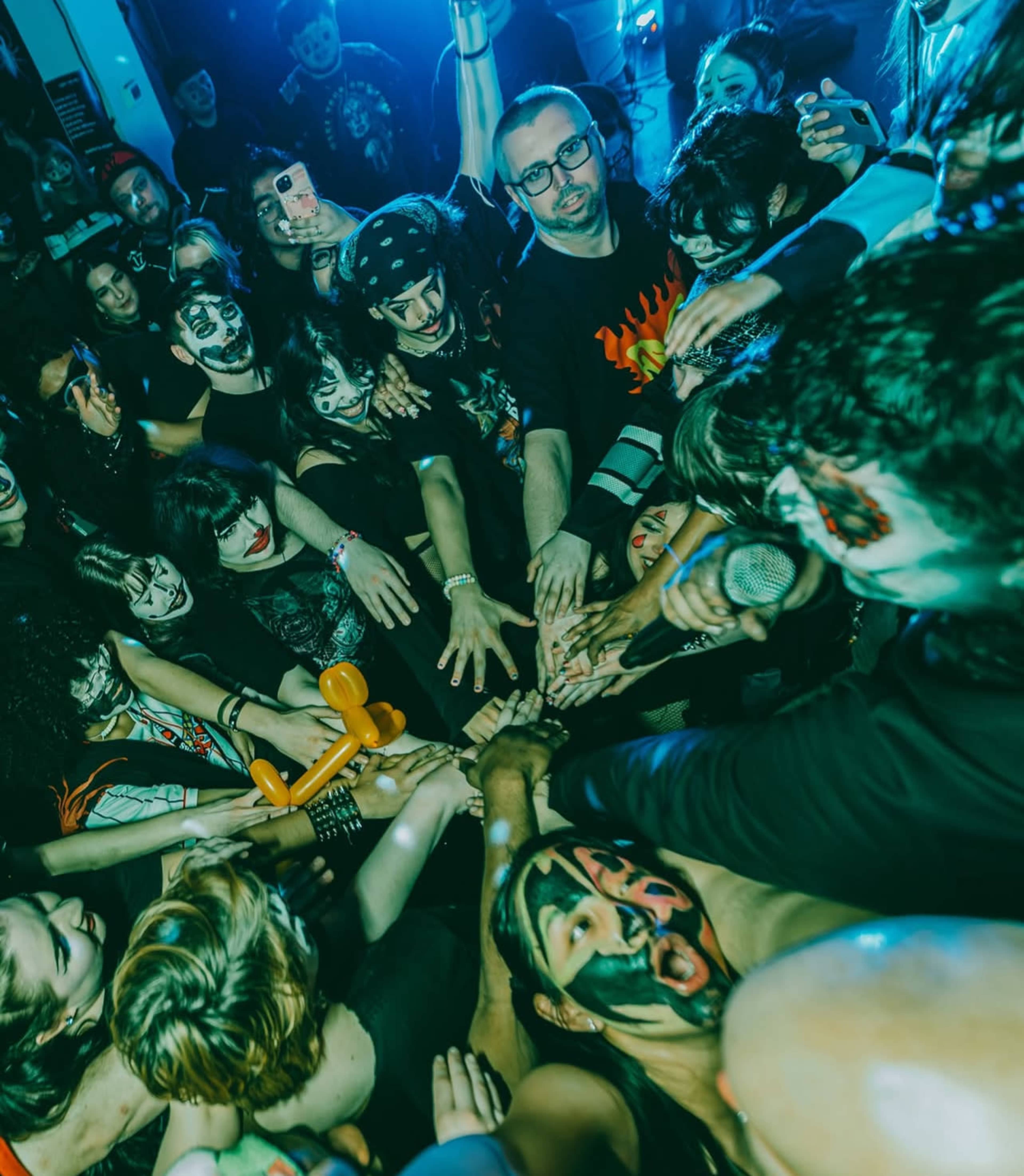 A crowd of people with face paint gathers around a performer, reaching out with their hands in a concert setting.
