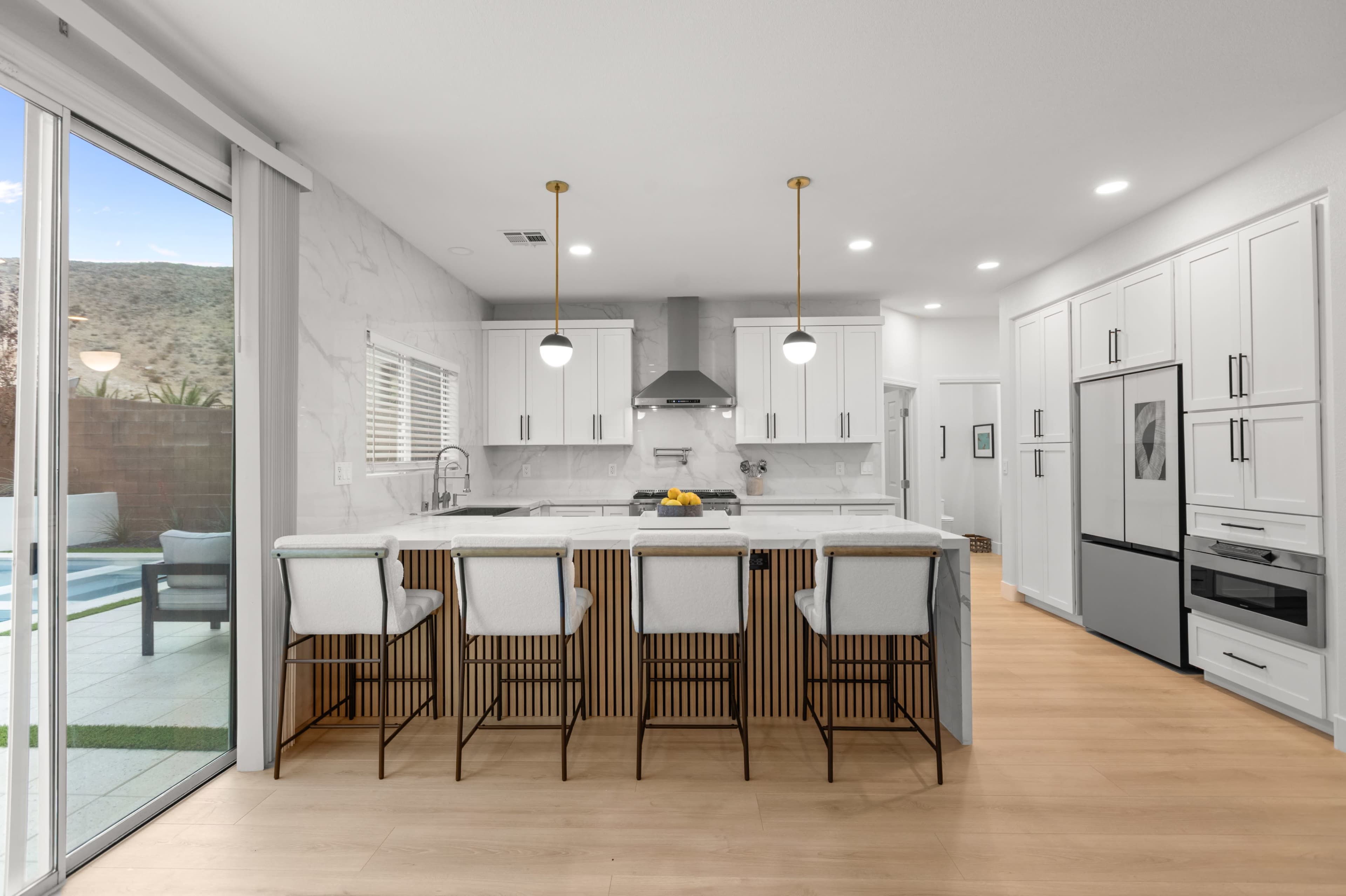 The image shows a modern kitchen with a large island and bar stools, featuring white cabinetry and a marble countertop.