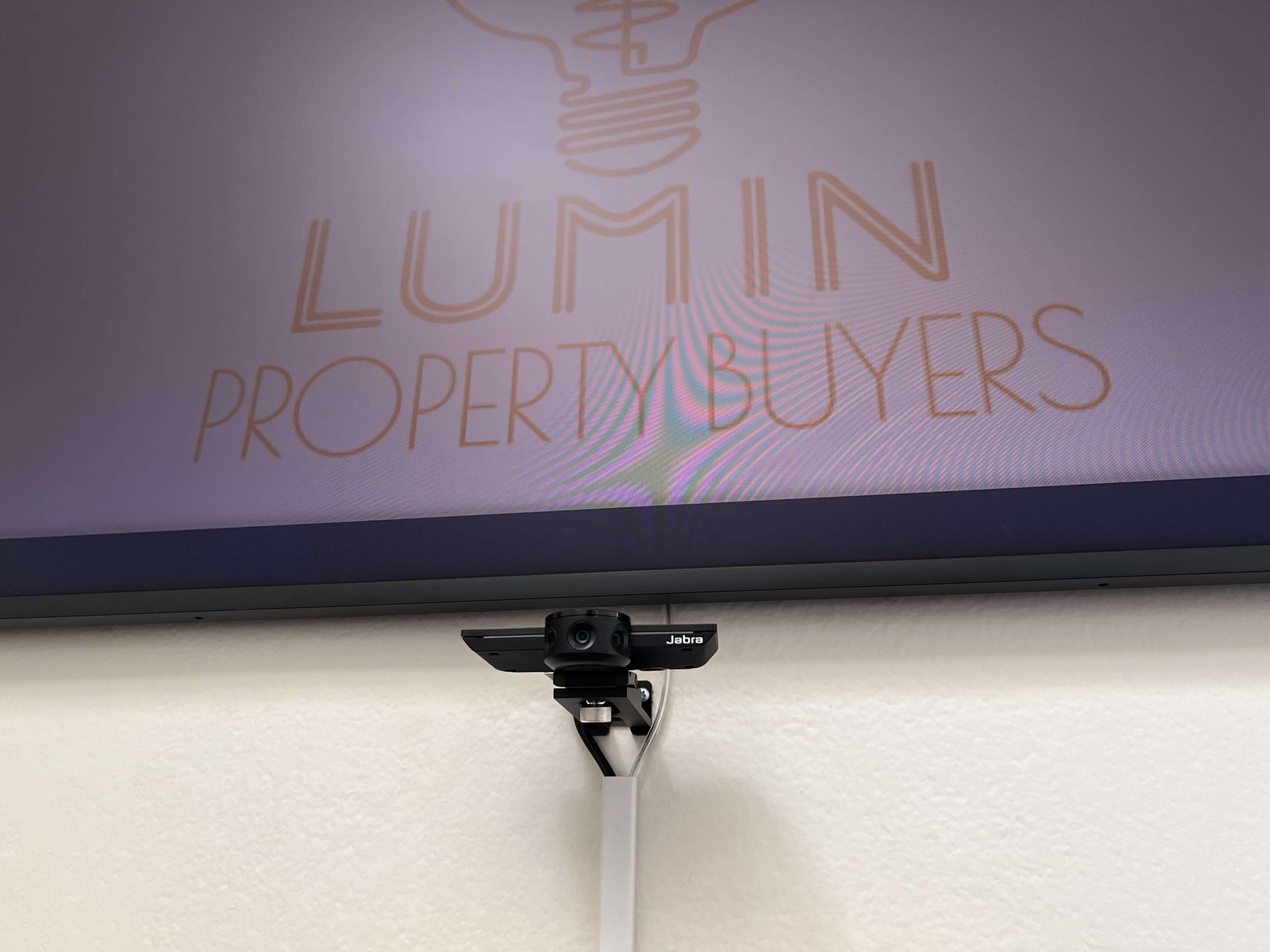 A webcam is mounted below a screen displaying the text "LUMIN PROPERTYBUYERS".