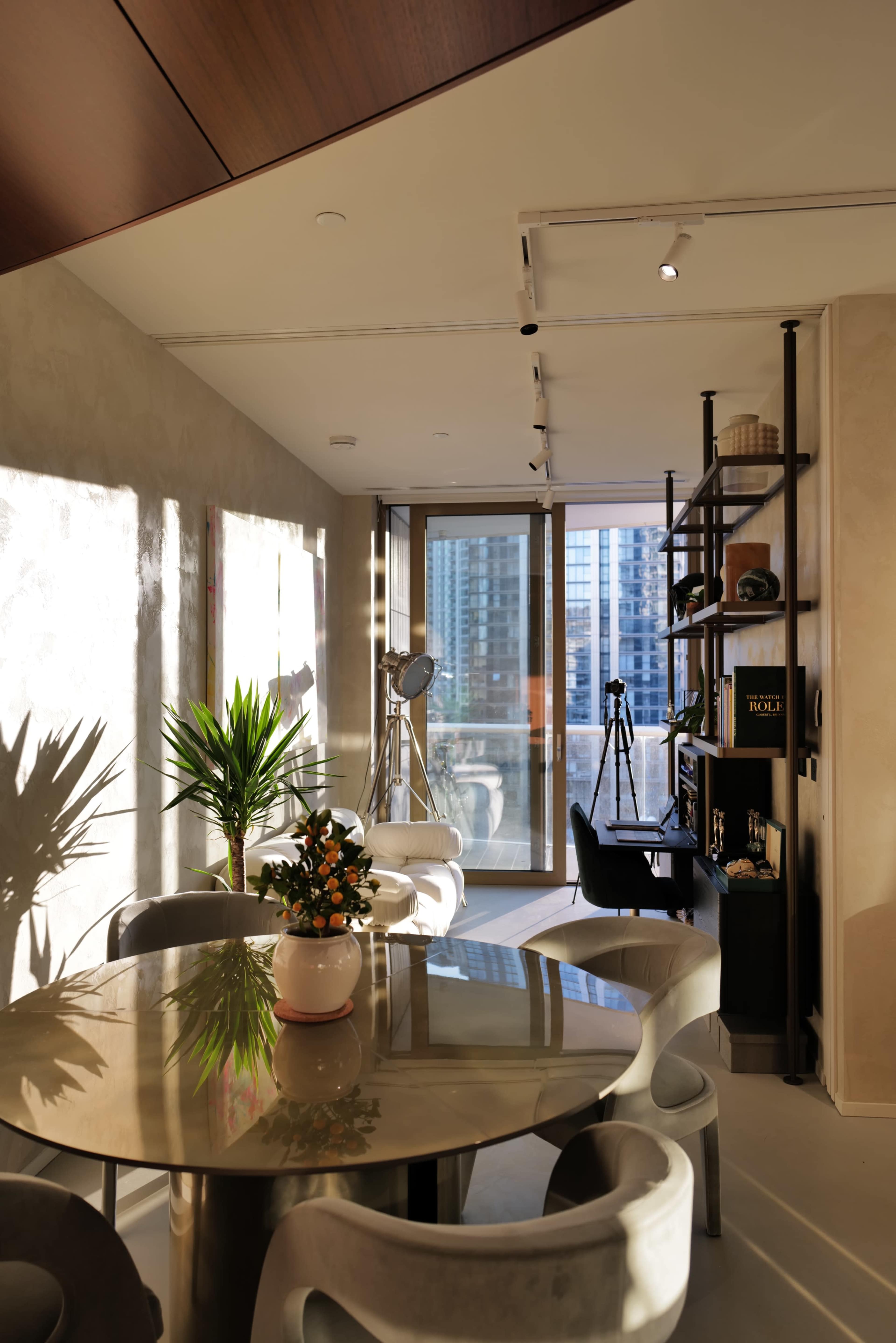 A modern interior space with a round dining table, chairs, and large windows overlooking a city skyline.