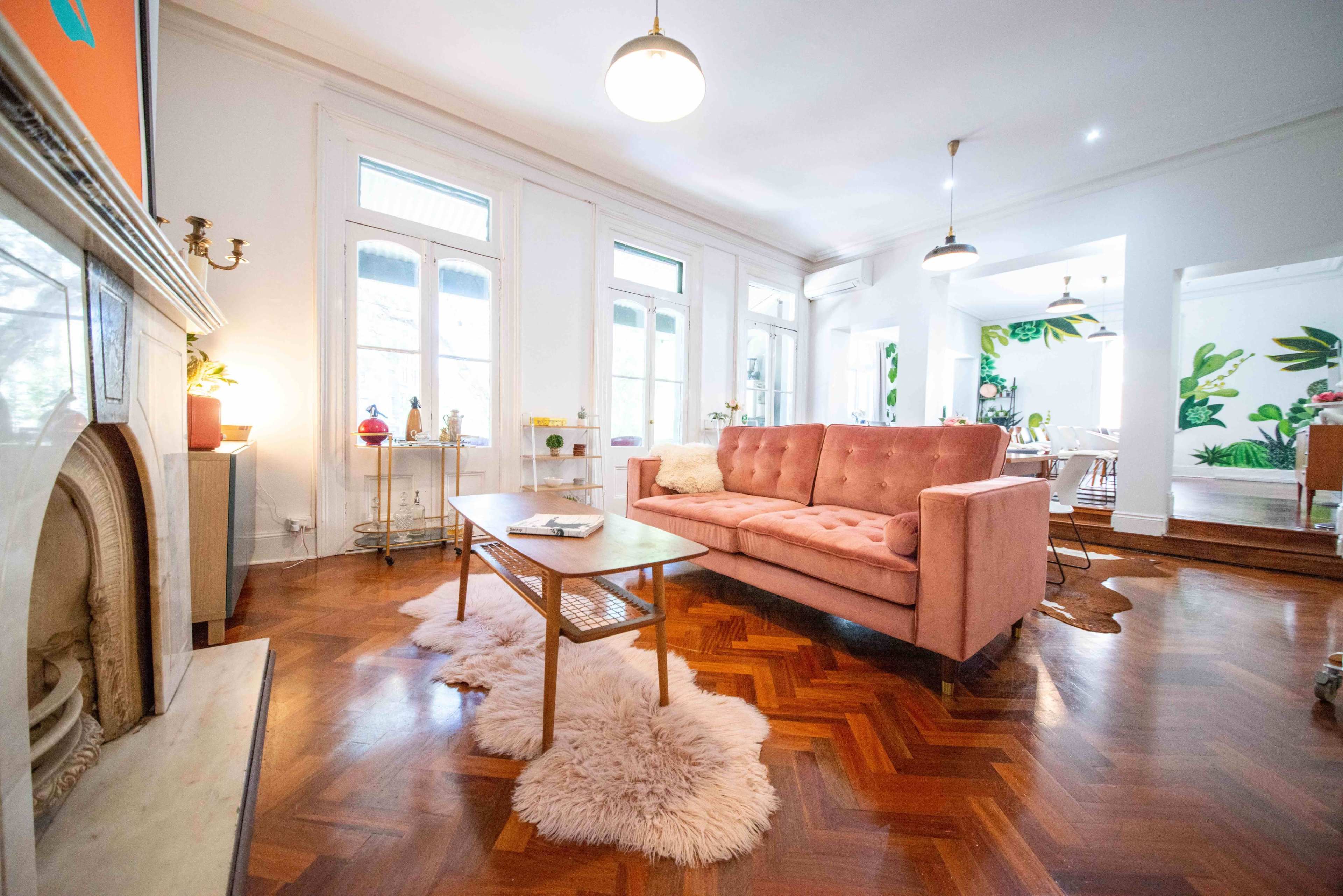 The living room features a pink sofa, a wooden coffee table, and a decorative fur rug, with large windows allowing natural light to fill the space.