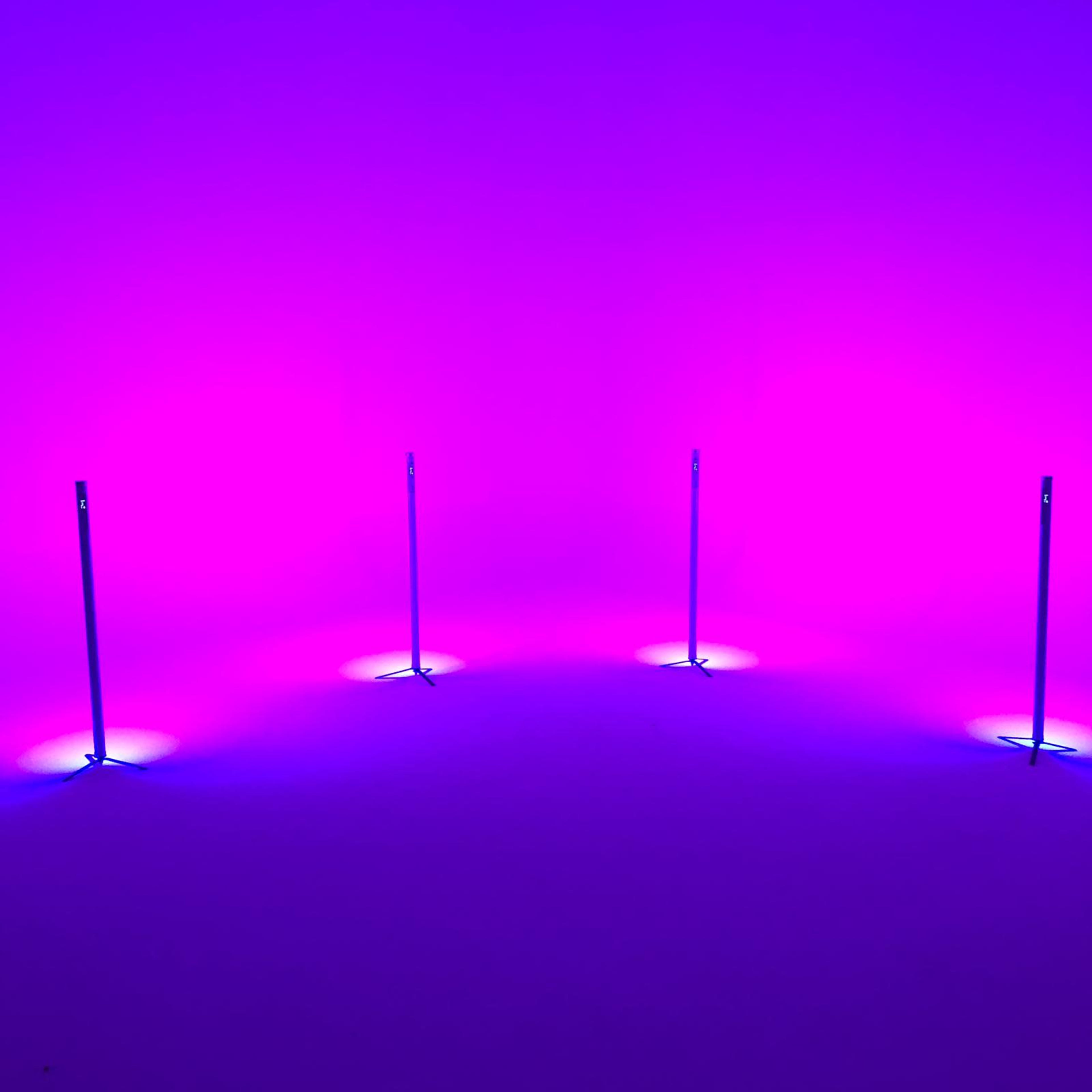 The image shows four vertical light poles arranged in a circular formation, illuminated by purple and blue ambient lighting.