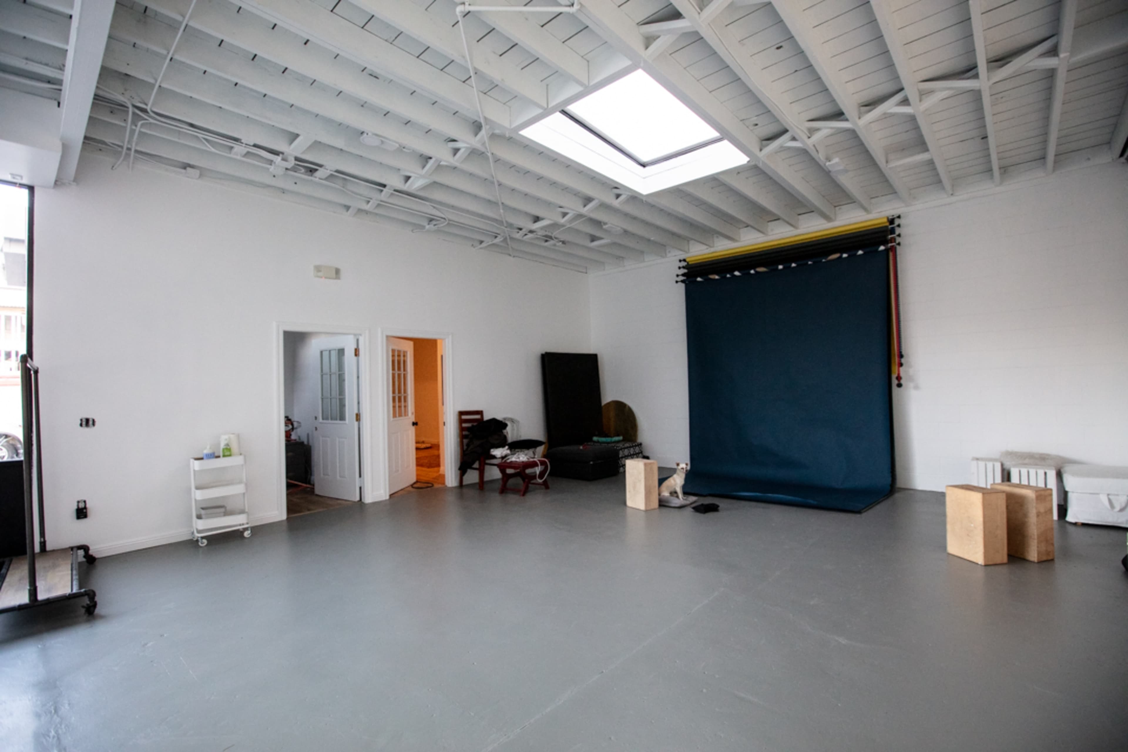 A spacious, well-lit studio with a blue backdrop, wooden blocks, and an open doorway leading to another room.