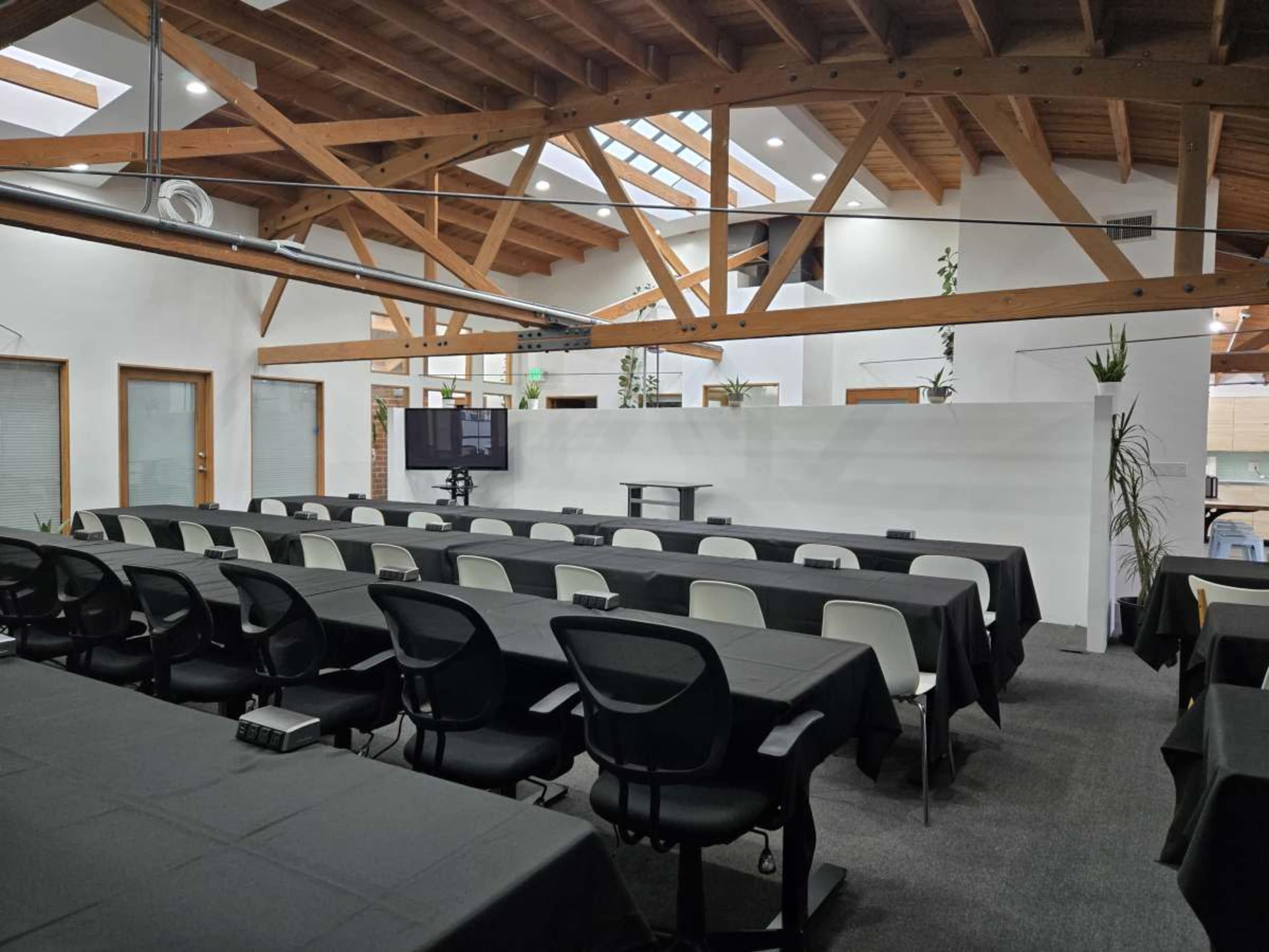 The image shows a spacious conference room with multiple rows of tables covered in black cloth, under a ceiling with exposed wooden beams and skylights.