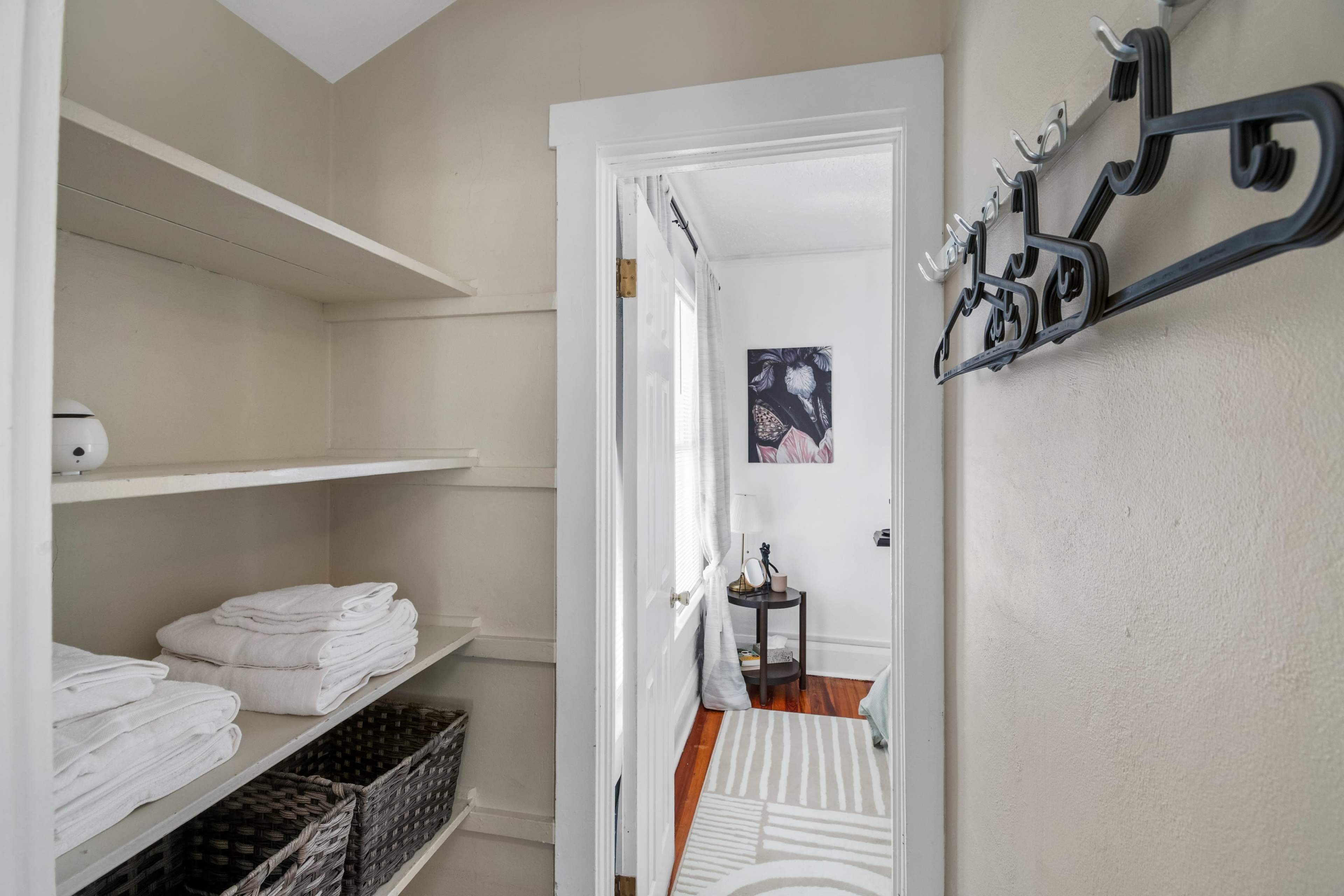 A narrow hallway leading to a room with shelves holding neatly stacked towels and hooks mounted on the wall.