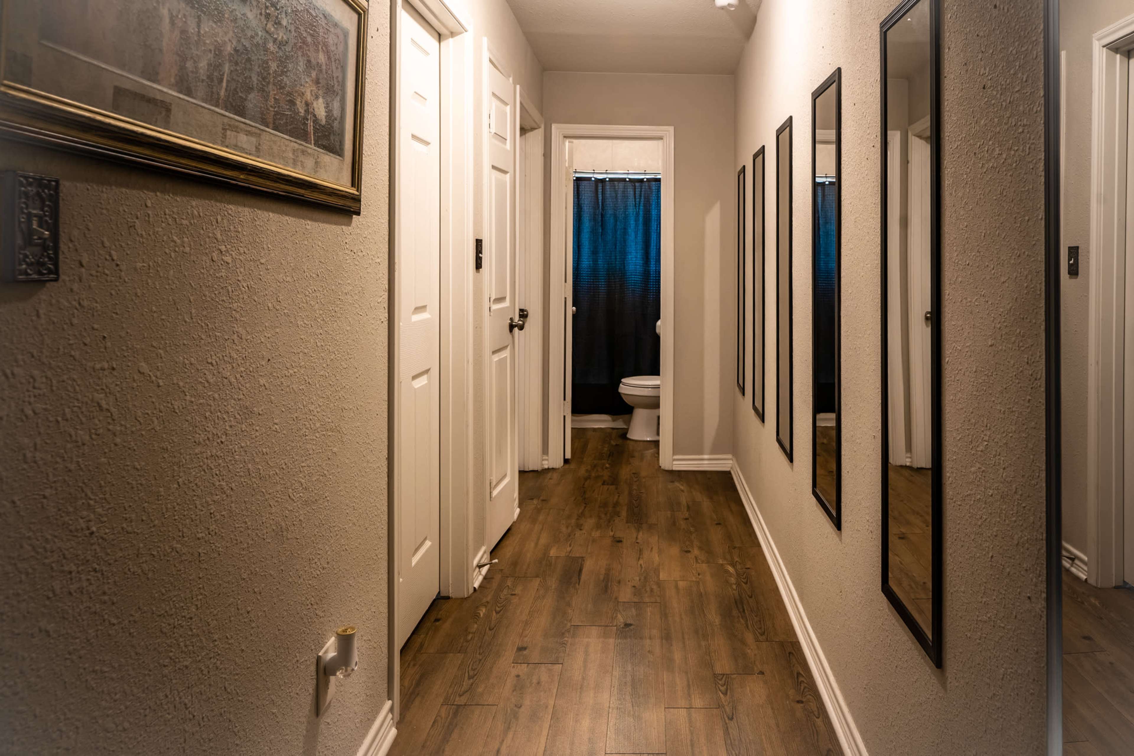 A narrow hallway features several mirrors along the walls, leading to a bathroom at the end.