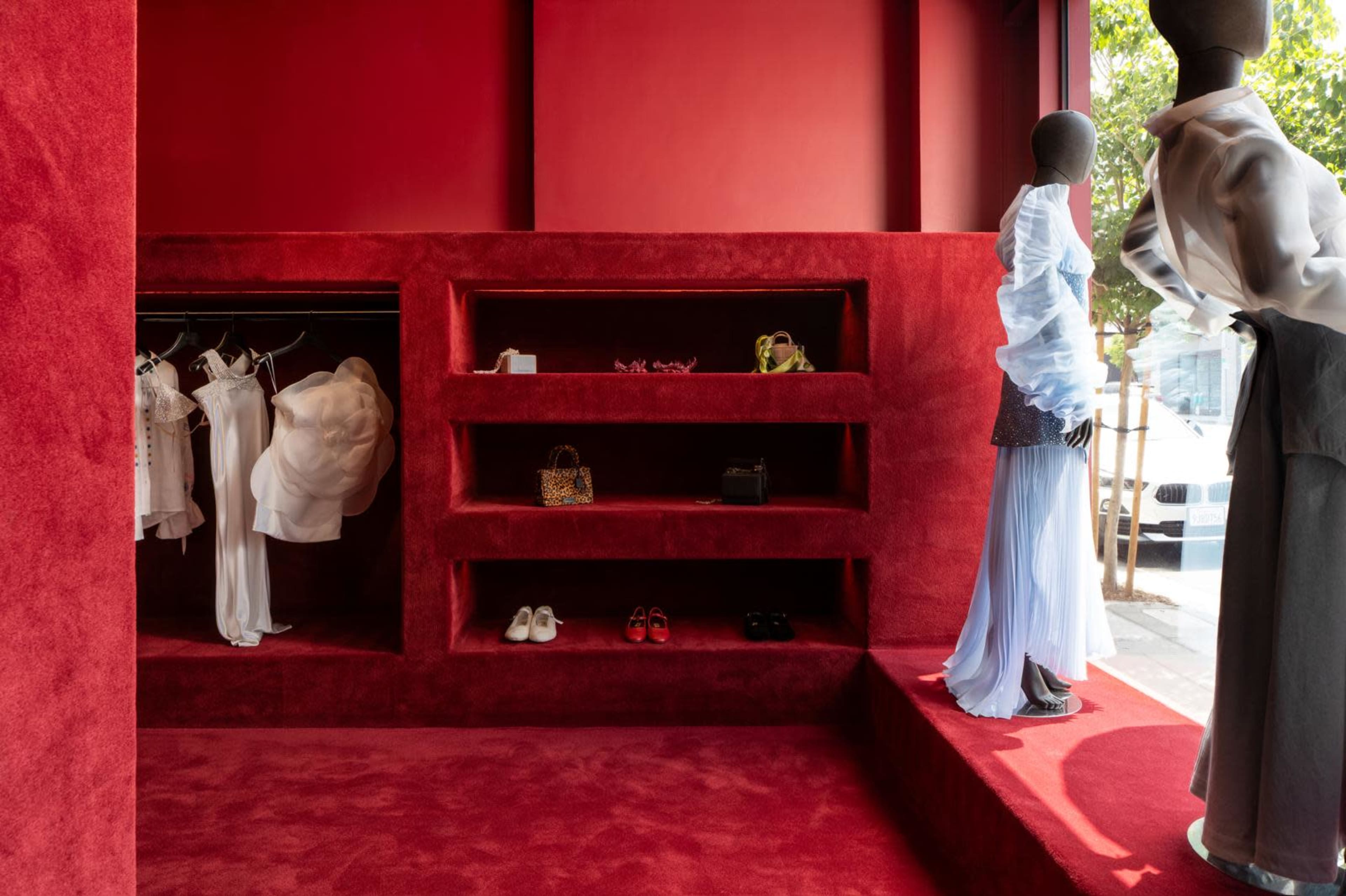 The image shows a red-themed boutique interior featuring mannequins displaying clothing and shelves with various fashion items.