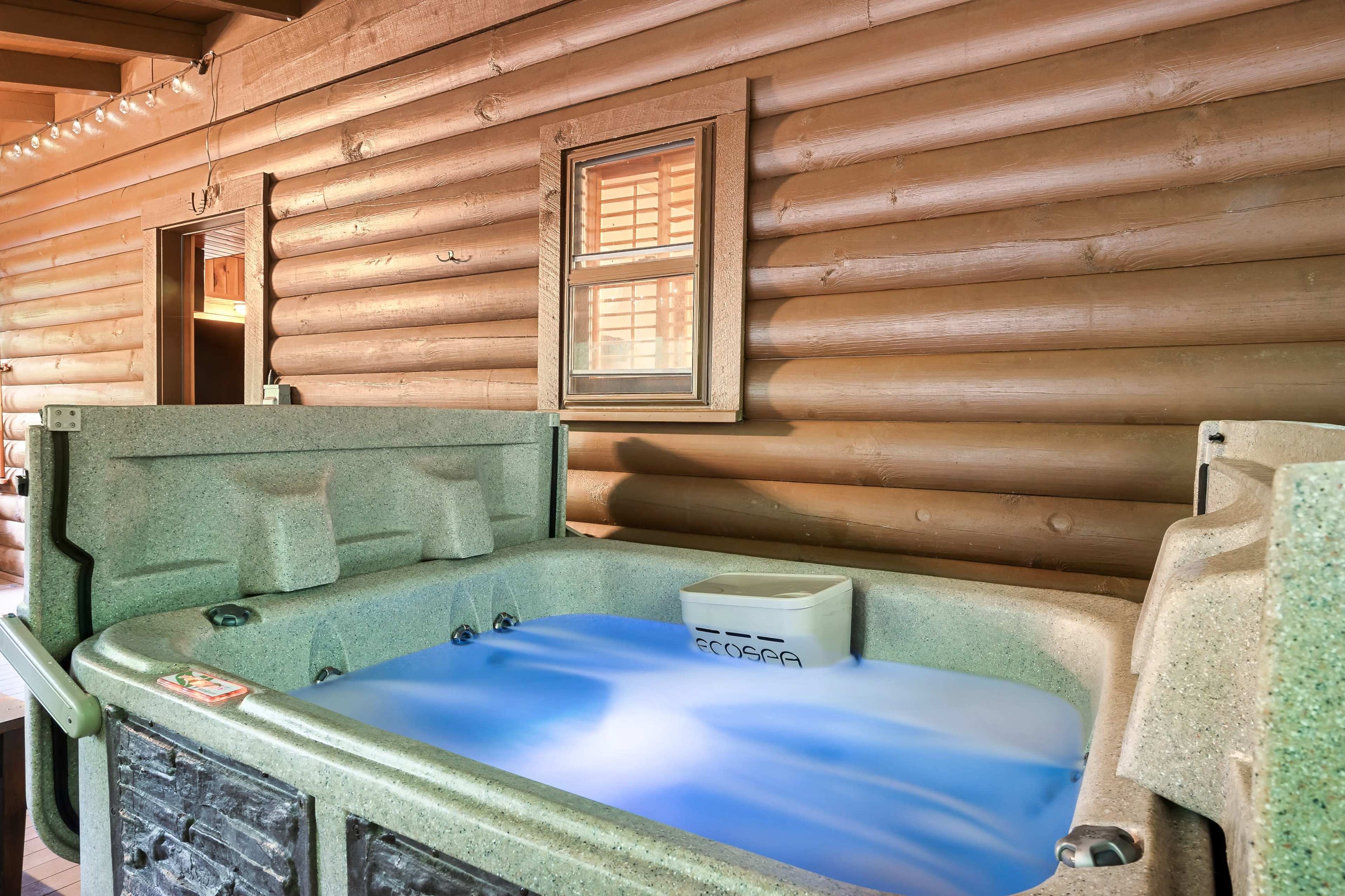 A hot tub filled with blue water is set against a backdrop of log cabin walls and a small window.
