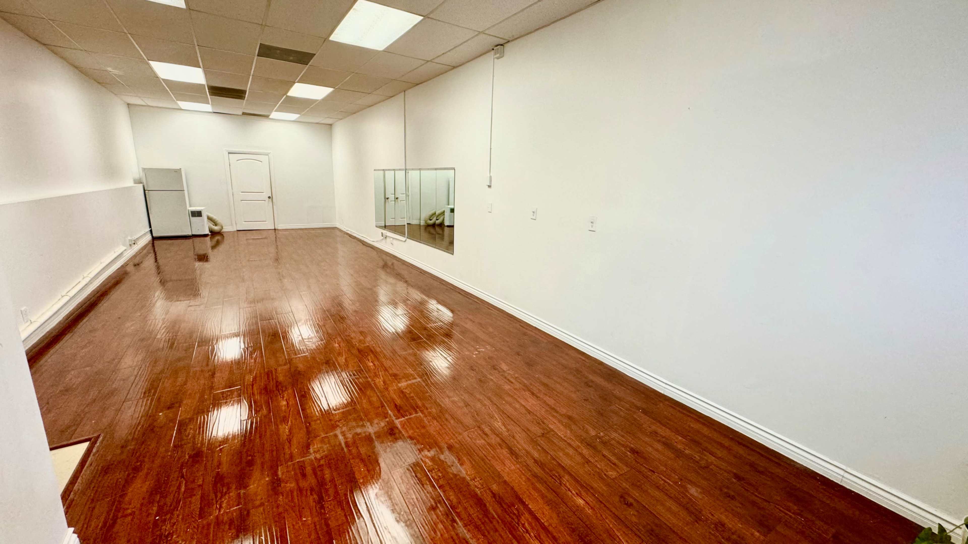 The room features polished wooden flooring and white walls, with a mirror on one side and a door leading to another space.