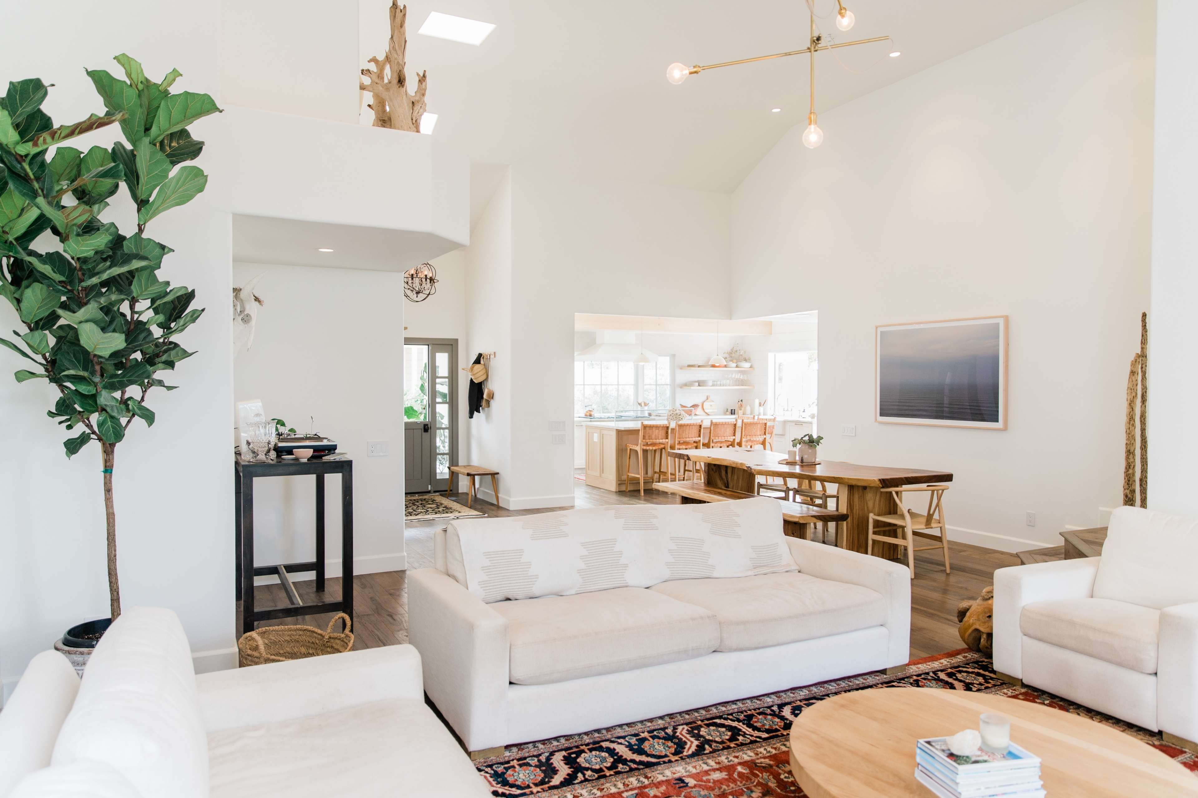 A modern, airy living space with white walls, light furniture, and a large dining area in the background.