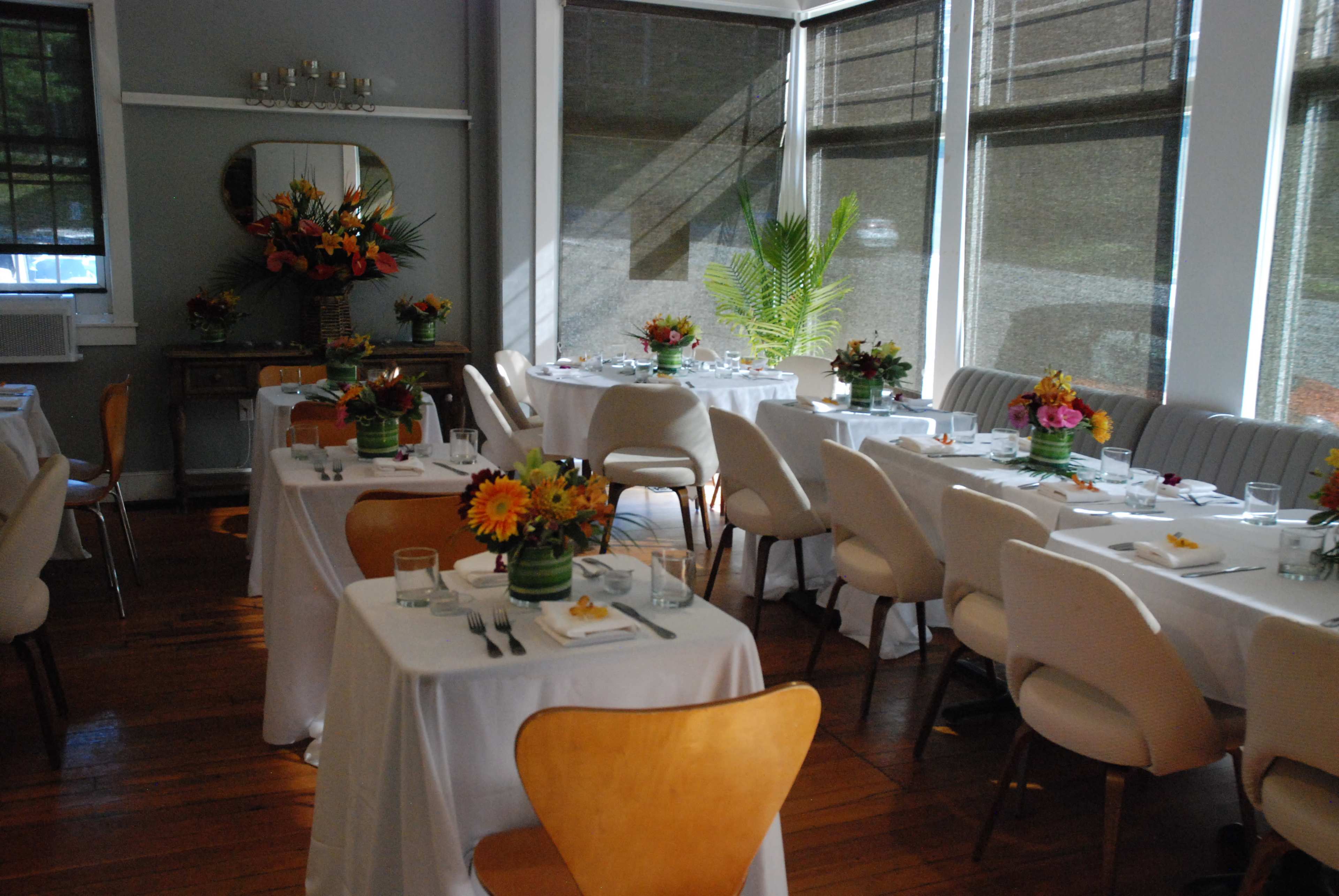 A bright, airy dining area with several tables set for a meal, each adorned with floral centerpieces.