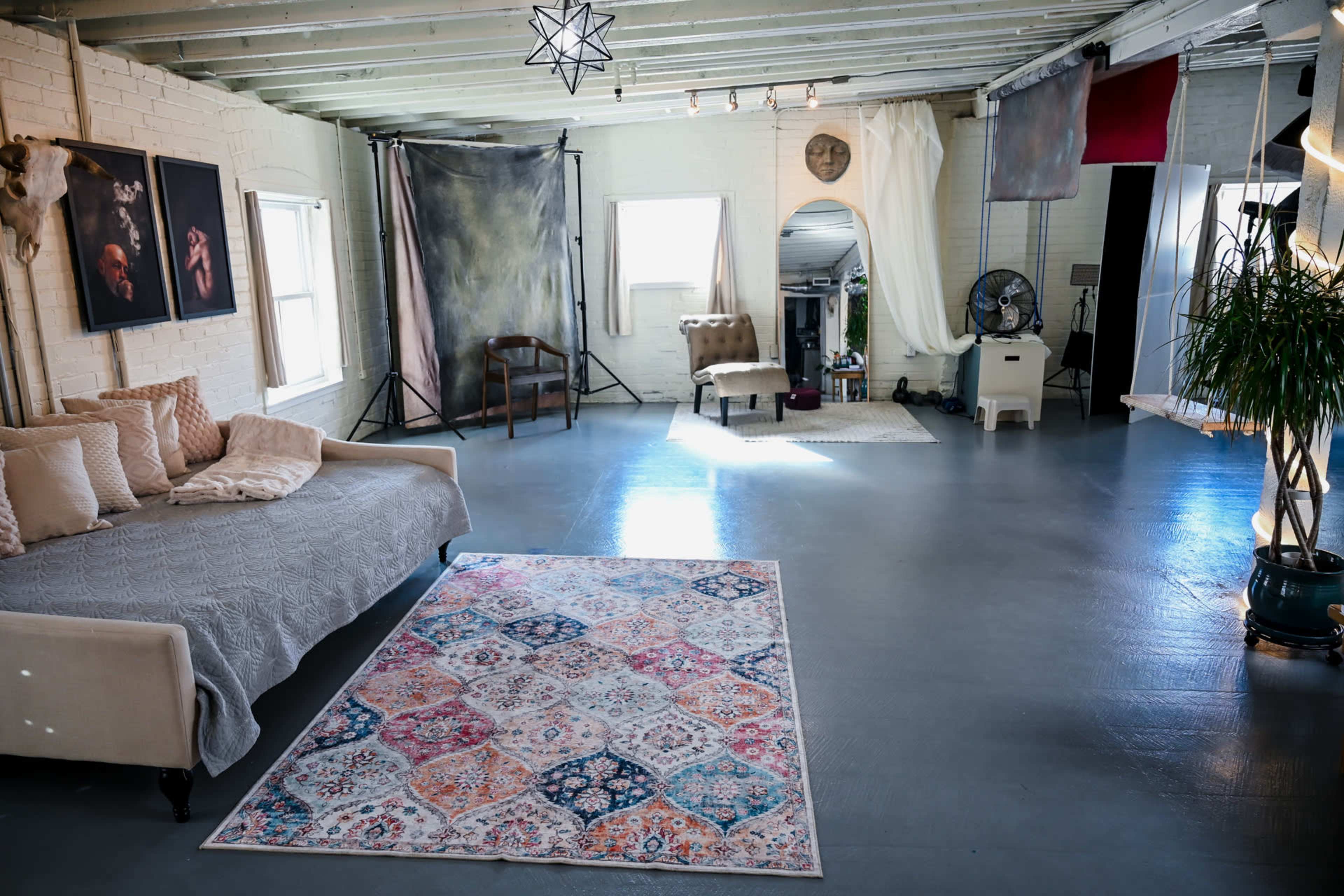 The image shows a large, well-lit studio space with a beige couch, photography backdrops, and various decorative elements.