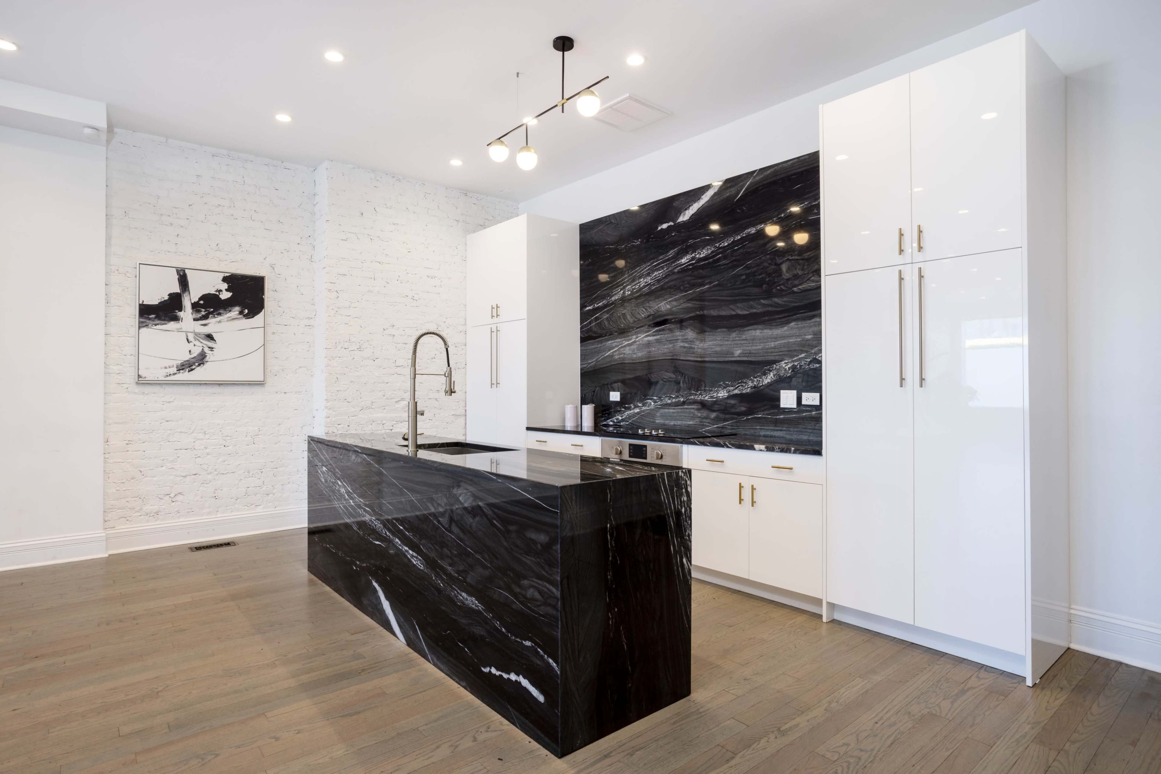 A modern kitchen featuring a black marble island with a sleek countertop and white cabinetry against a textured white brick wall.