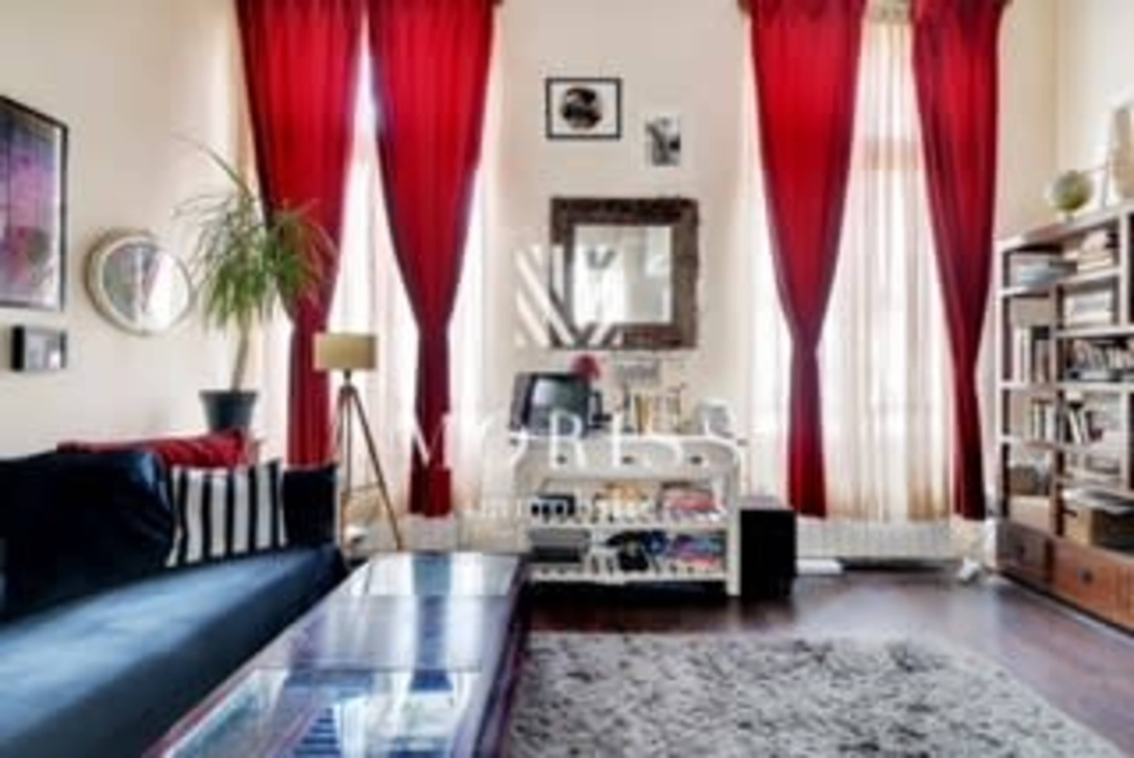 The image shows a living room with red drapes, a dark couch, a bookshelf, and a decorative mirror on the wall.