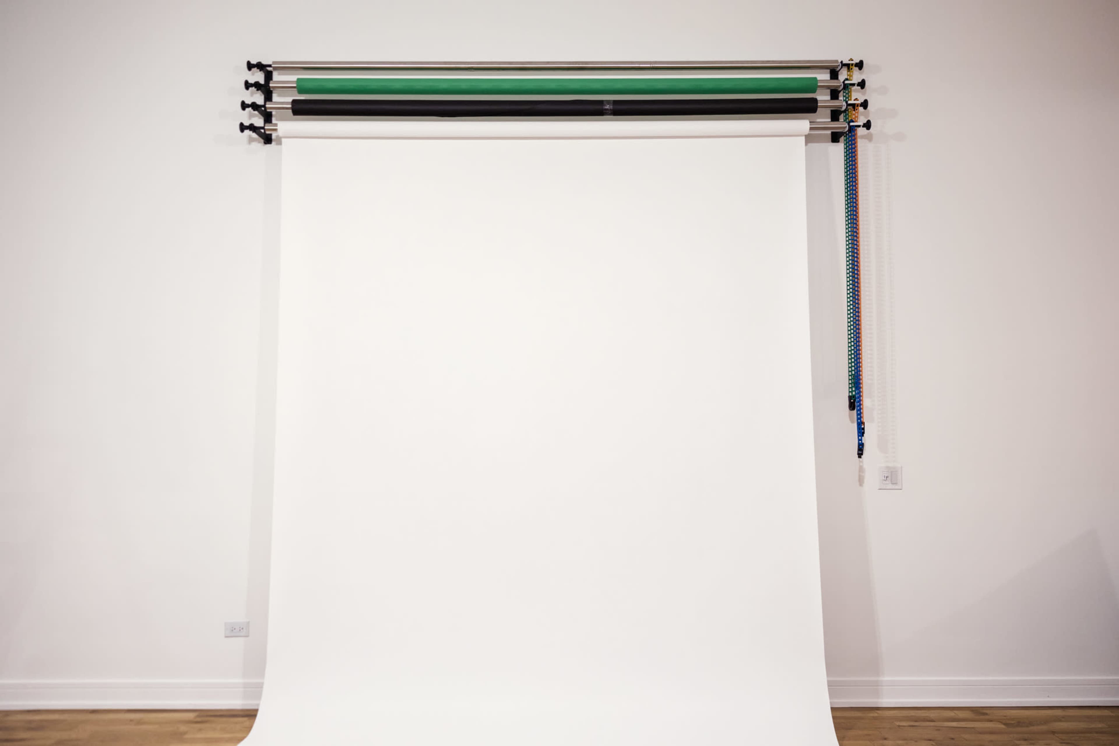 A blank photography backdrop is suspended from a rack against a plain wall.