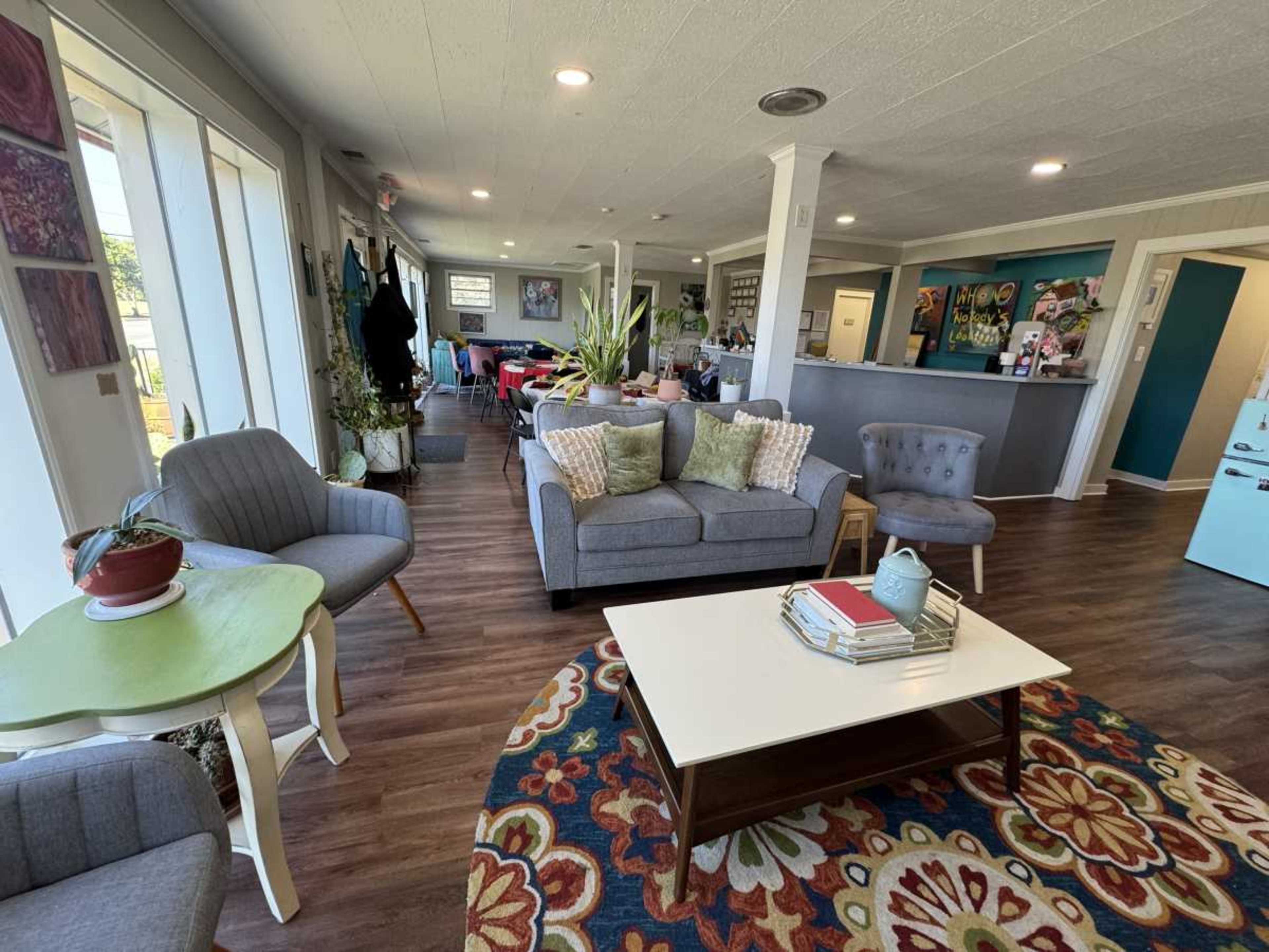 The image shows a spacious, brightly lit living area with a mix of comfortable seating arrangements, a coffee table, and decor on the walls.