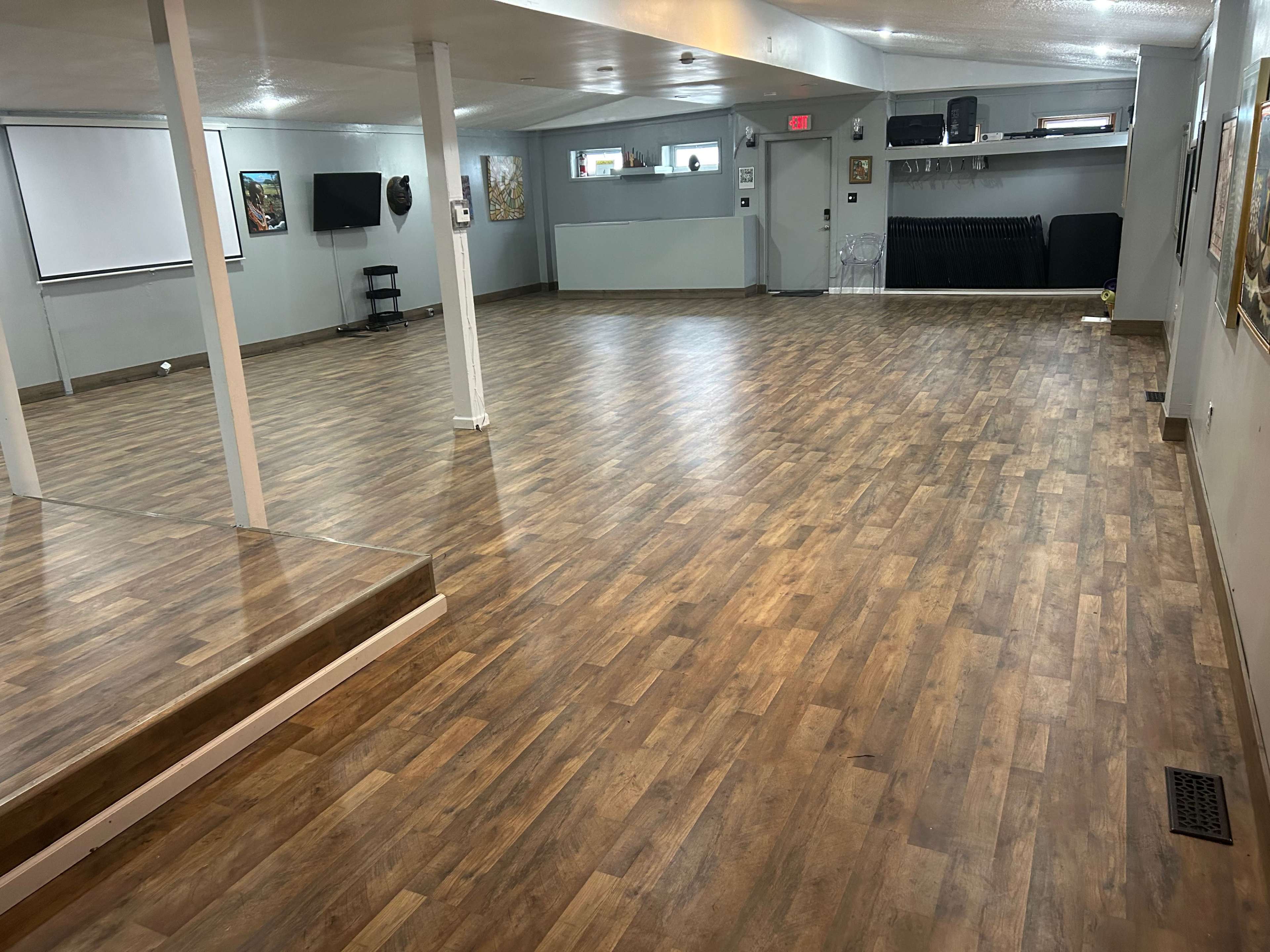 A spacious, empty room with wooden flooring, equipped with a projector and a large screen on one wall.
